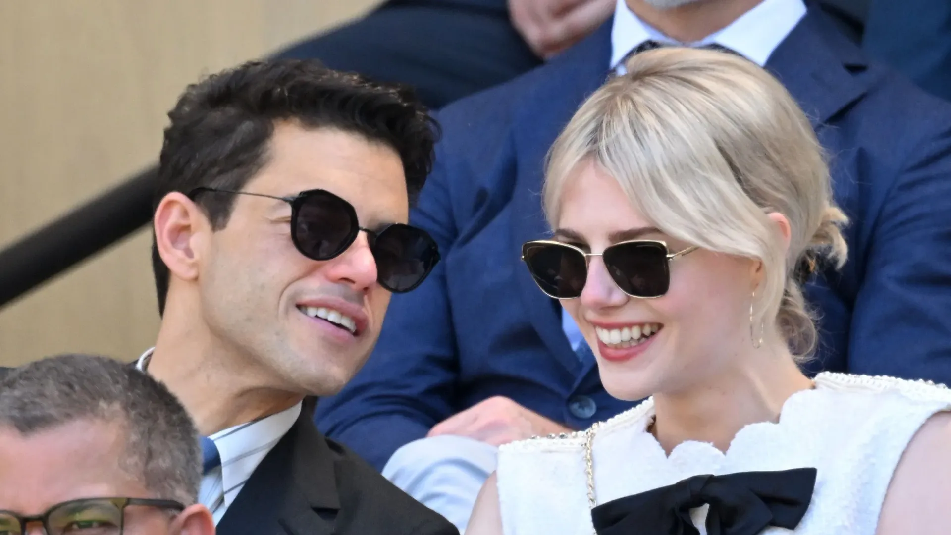 Un hombre y una mujer con gafas de sol están sentados en las gradas del estadio