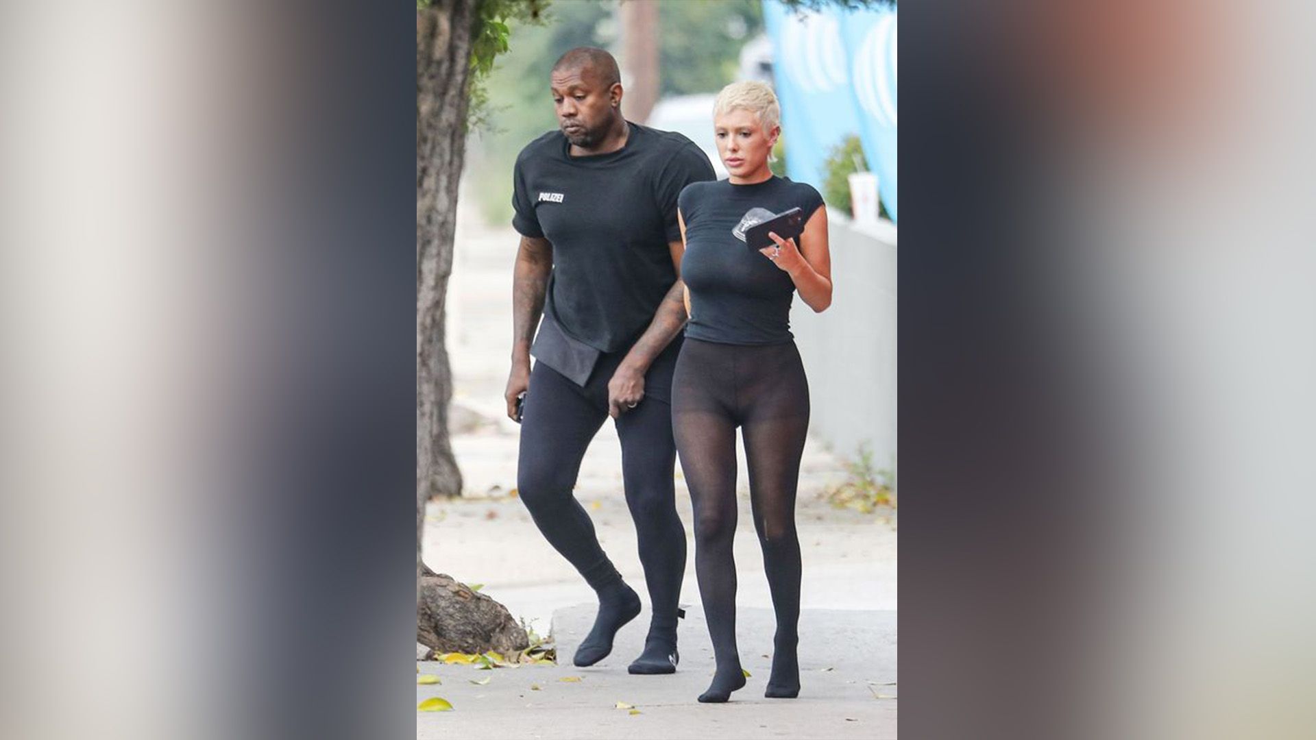 Un hombre de piel oscura de negro y una mujer rubia con una camiseta negra y medias transparentes negras