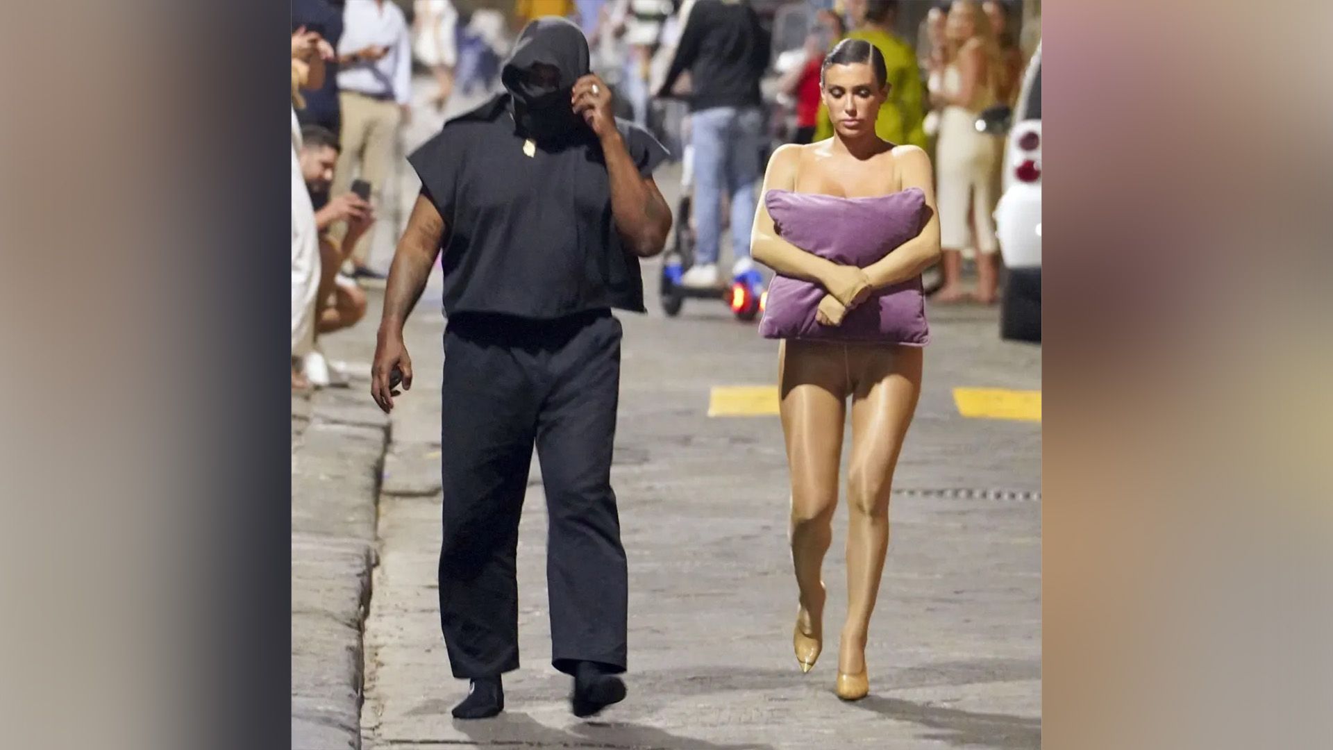 Un hombre de piel oscura de negro y una chica con un mono color carne y una almohada lila en sus manos