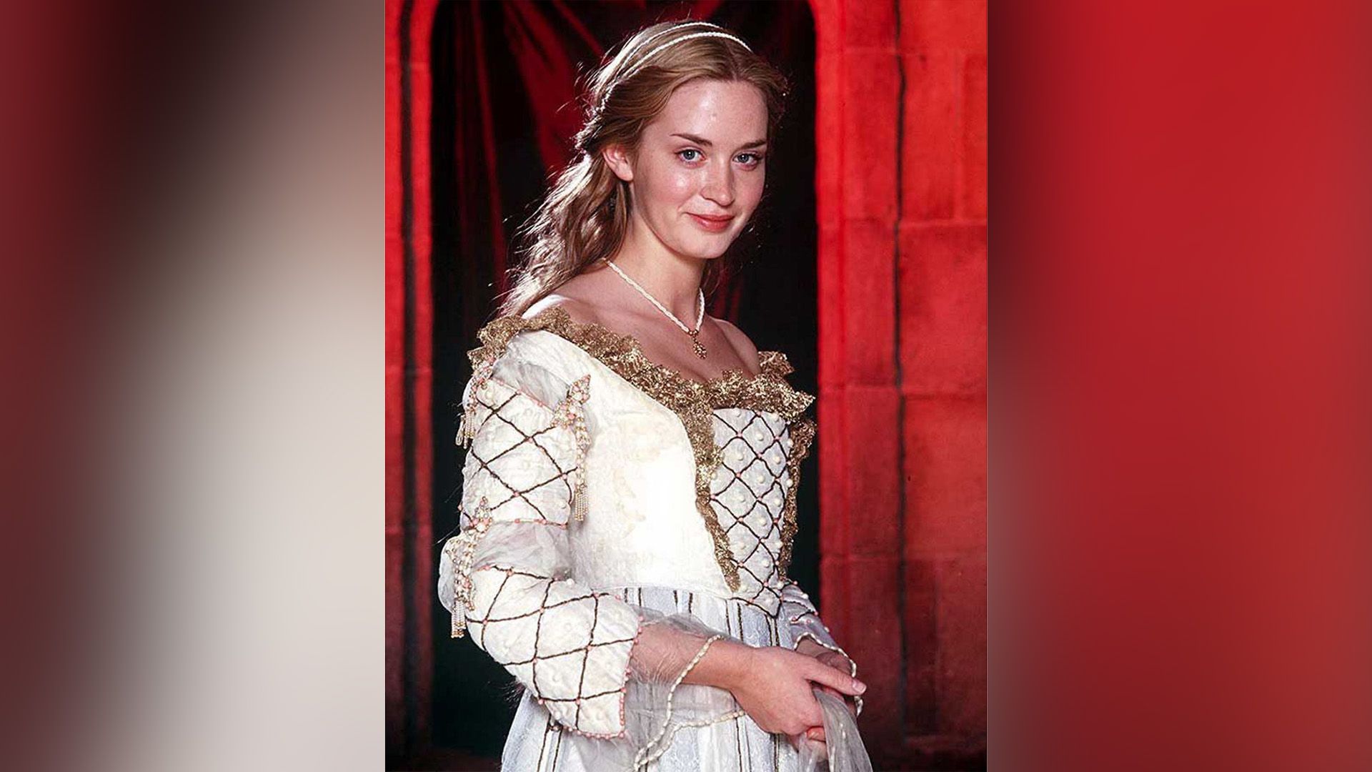 Una joven rubia con un vestido histórico blanco contra un fondo rojo