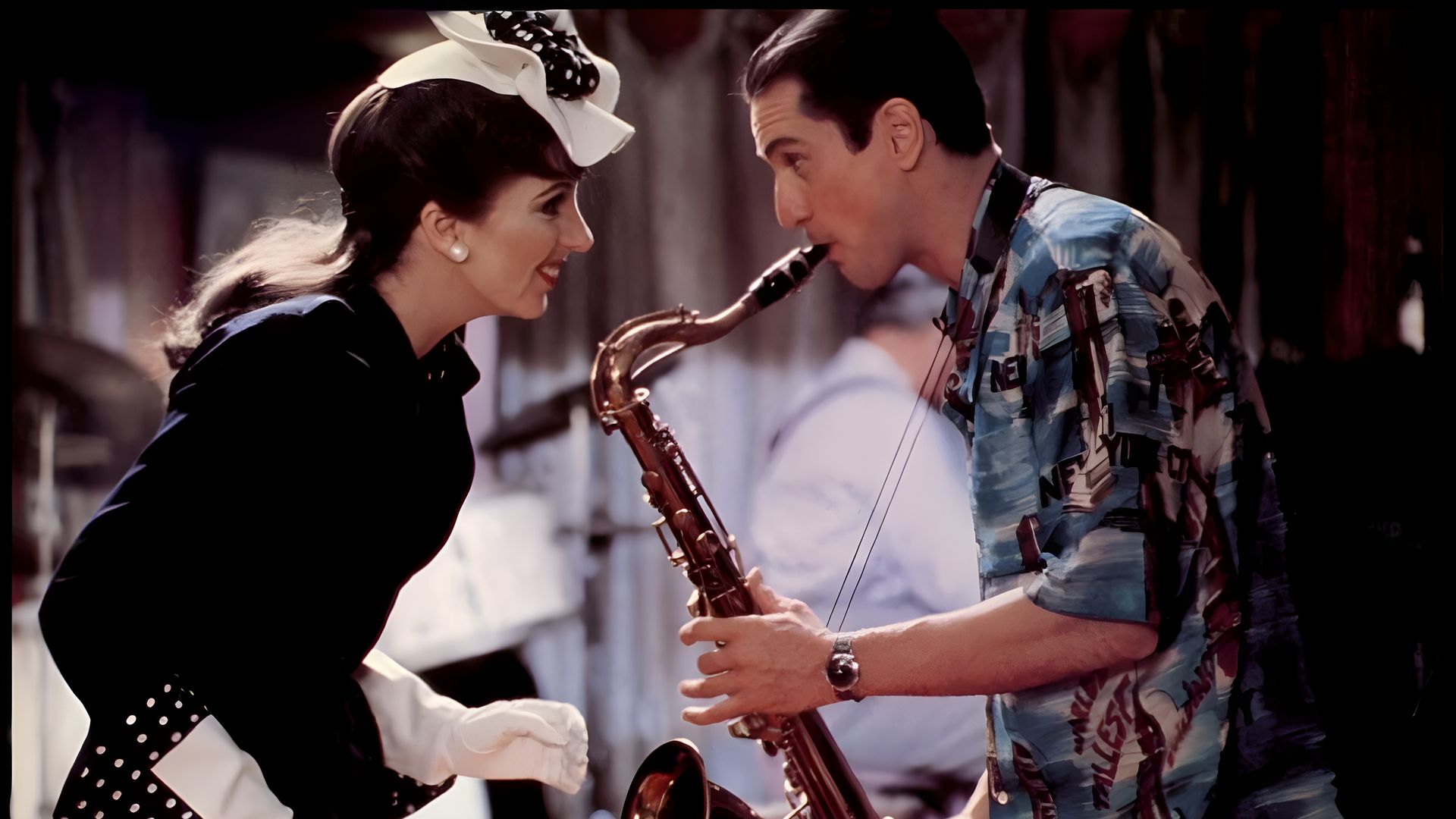 Un hombre con una camisa hawaiana tocando el saxofón, inclinándose hacia una mujer con un atuendo retro, guantes blancos y un sombrero