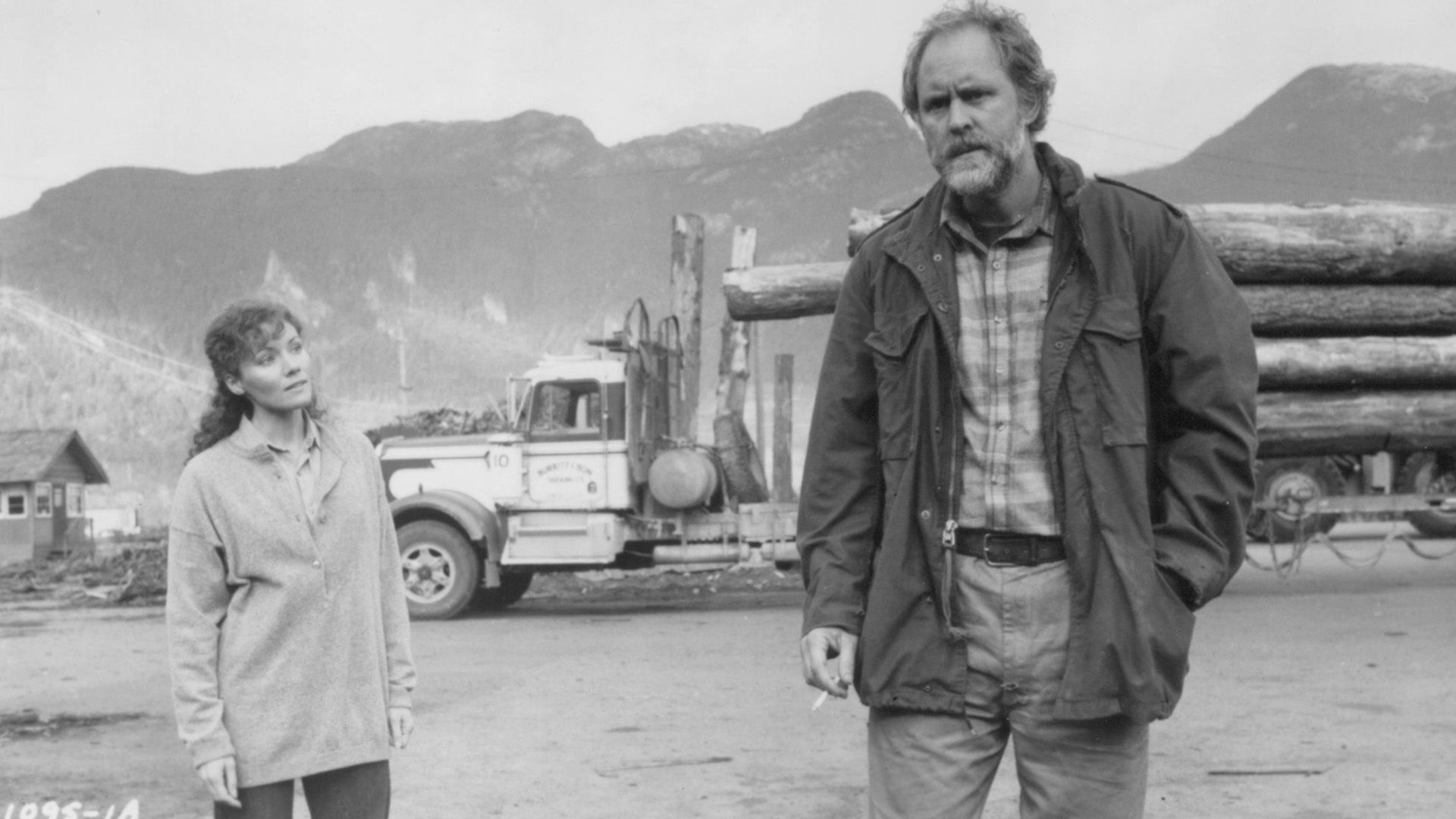 John Lithgow con ropa desgarrada frente a un camión maderero en una escena de la película "Distant Thunder"