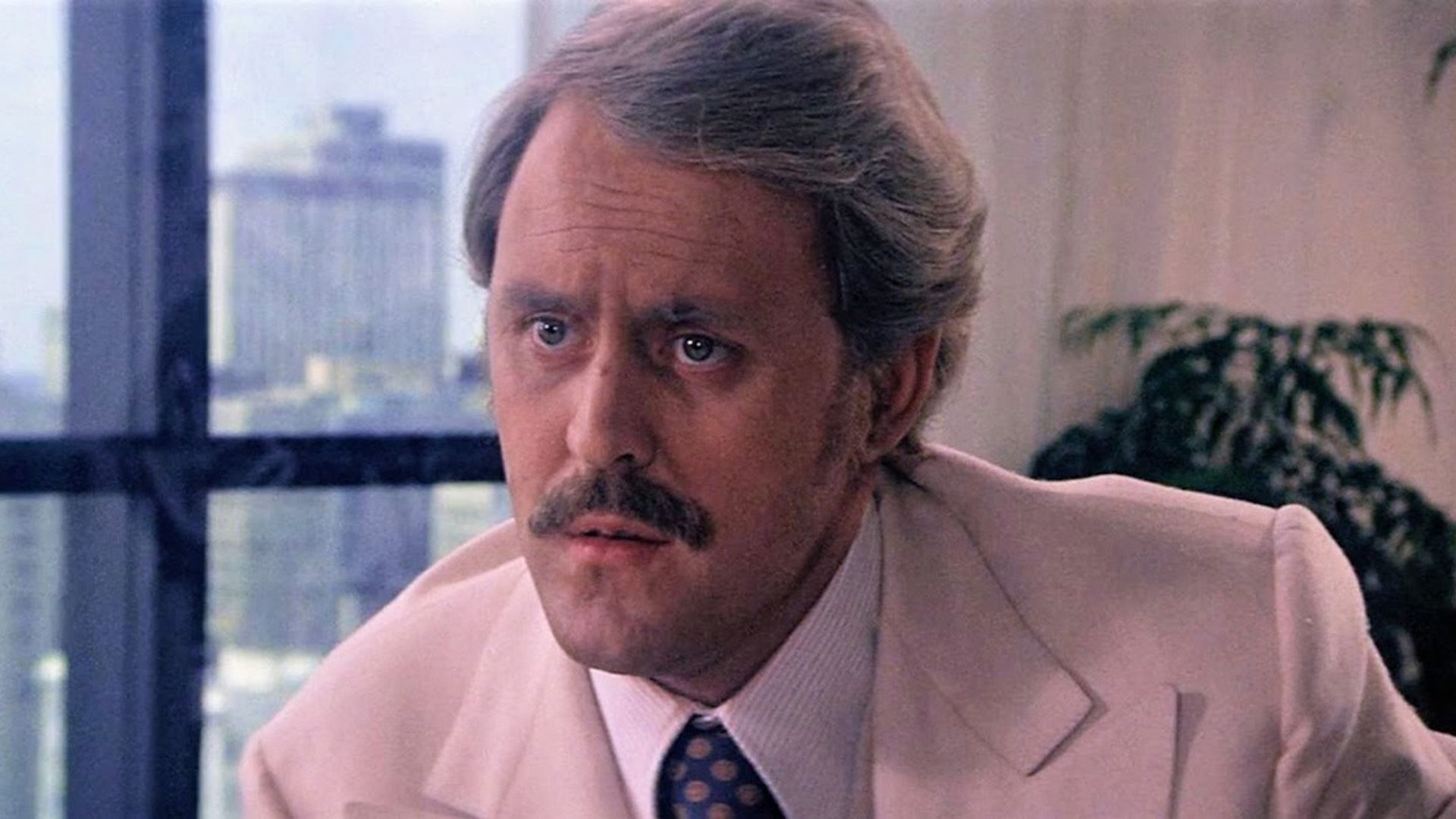 John Lithgow con bigote y chaqueta crema en una escena de la película "Obsession"