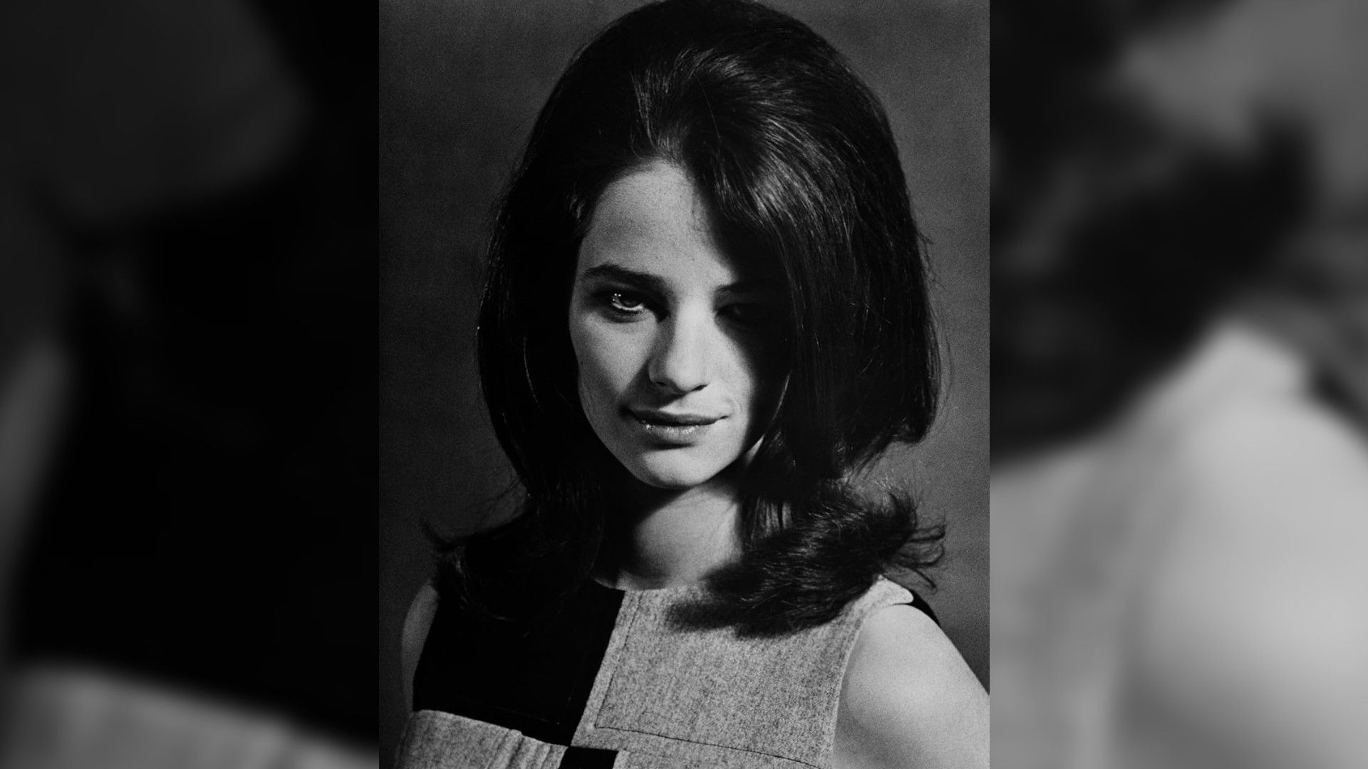 Un retrato en blanco y negro de la joven Charlotte Rampling con cabello grueso y una sonrisa misteriosa, vestida con un vestido de patrón geométrico.