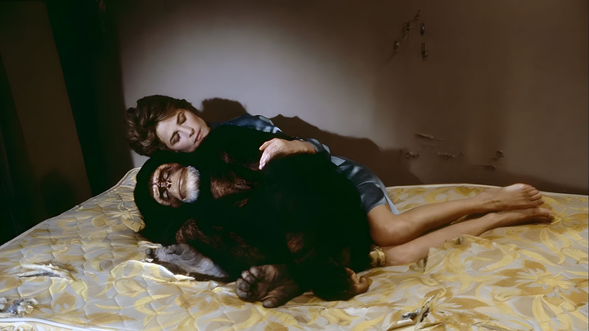 Charlotte Rampling en un vestido azul yace en un viejo colchón, abrazando a un chimpancé, en una habitación con paredes descascaradas