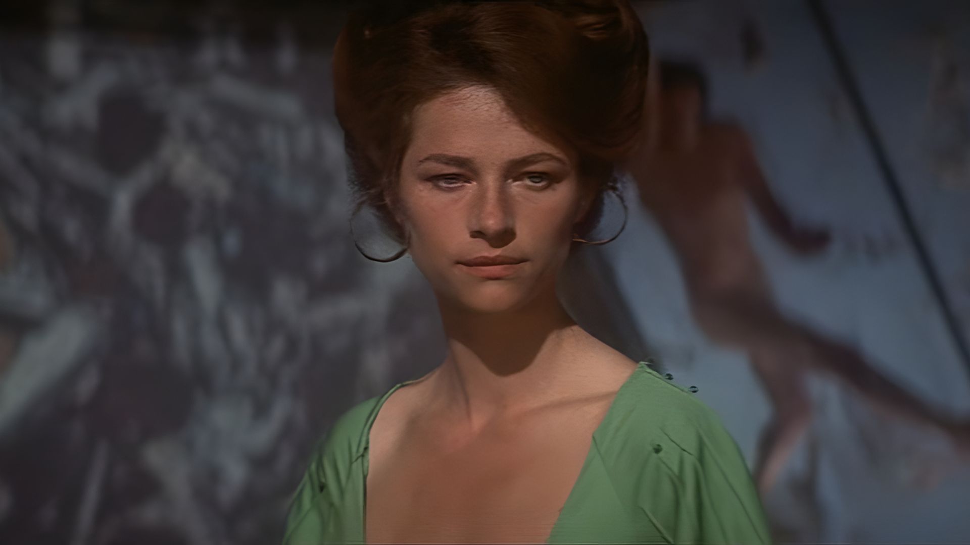 Joven Charlotte Rampling con un vestido verde y el cabello recogido contra un fondo difuminado con las figuras de personas