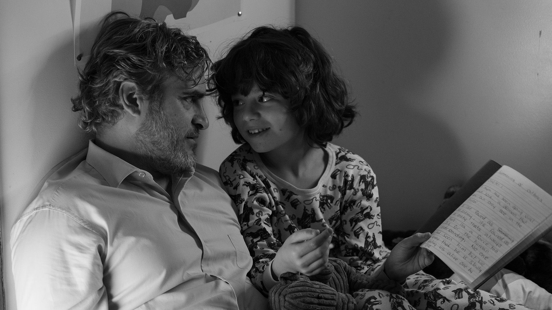Joaquin Phoenix y un niño pequeño están hablando, el niño sostiene un cuaderno