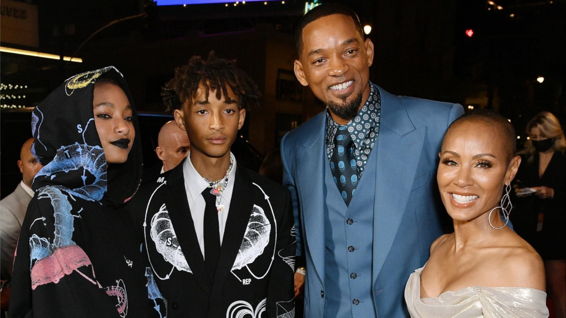 Will Smith en un traje azul sonríe a la cámara y abraza a su esposa, hija e hijo
