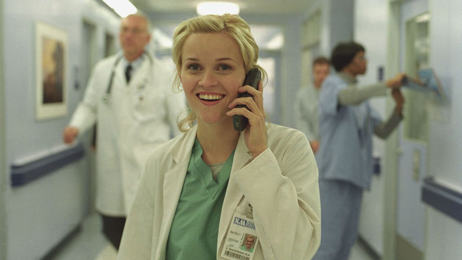 Reese Witherspoon alegre con uniforme de enfermera habla por teléfono en un pasillo del hospital
