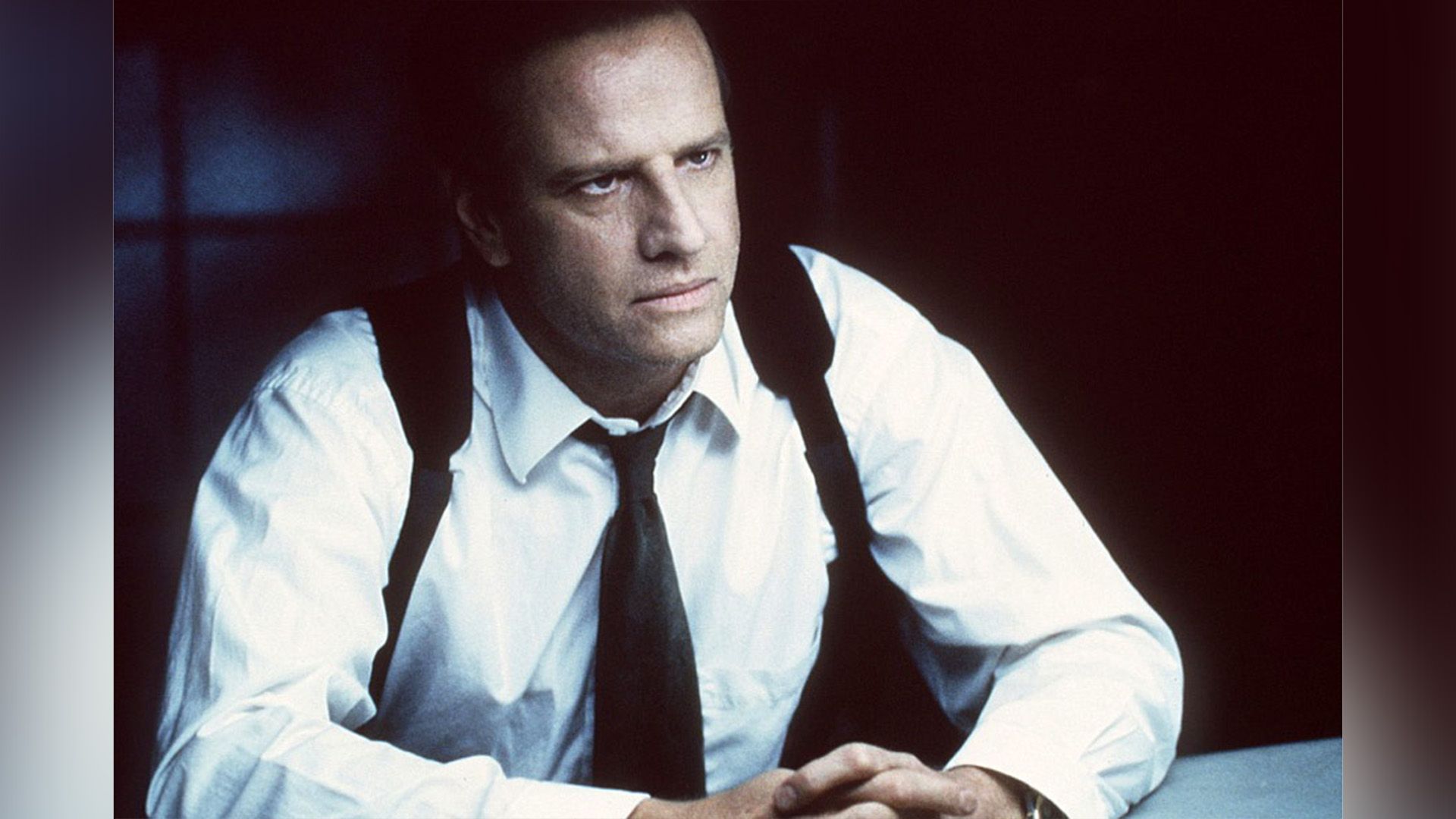 Christopher Lambert como detective sentado en la mesa