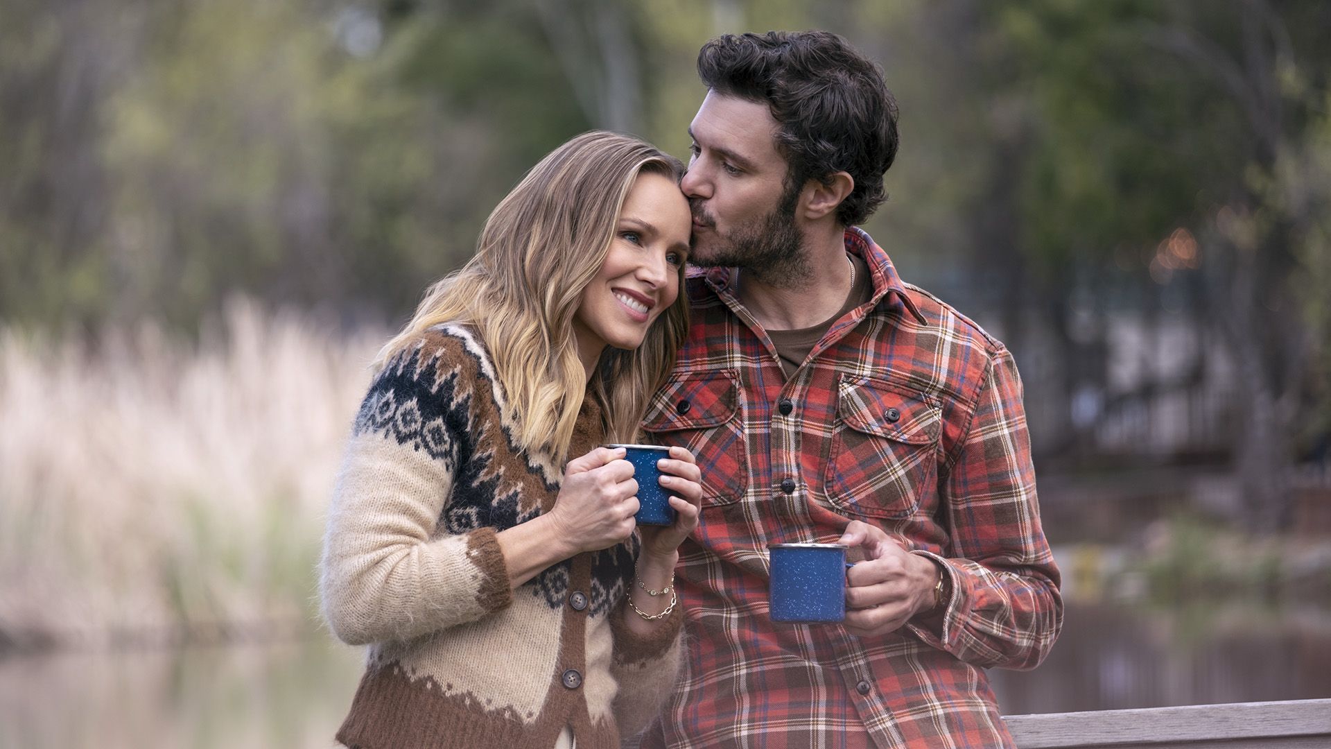 Kristen Bell apoya su cabeza en el hombro de Adam Brody, él le besa la frente, ambos sosteniendo tazas azules