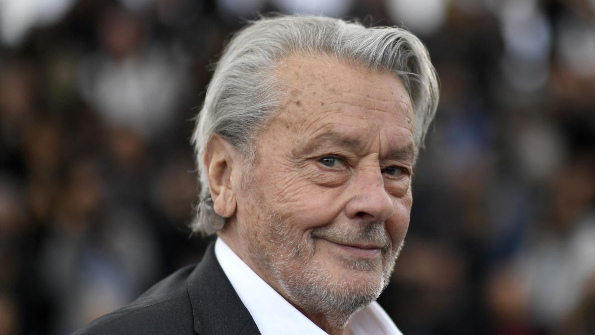 Un primer plano del actor sonriente Alain Delon contra un fondo borroso