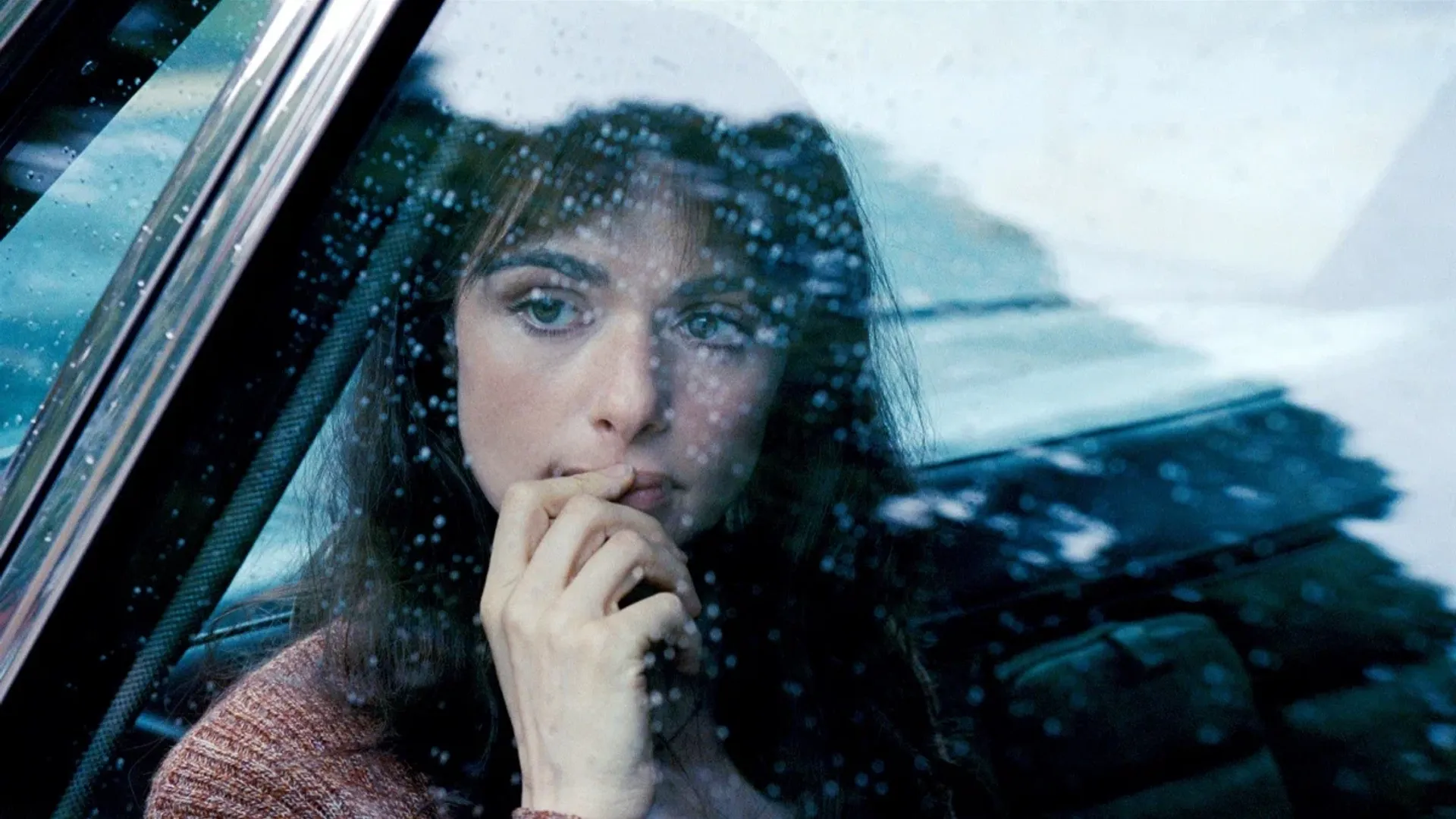 Primer plano del rostro de la actriz Rachel Weisz filmado a través del cristal de un auto bajo la lluvia