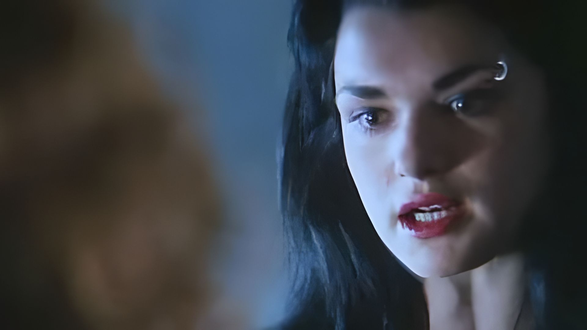 Un primer plano del rostro de Rachel Weisz, lleva un lápiz labial rojo brillante y un piercing en la ceja