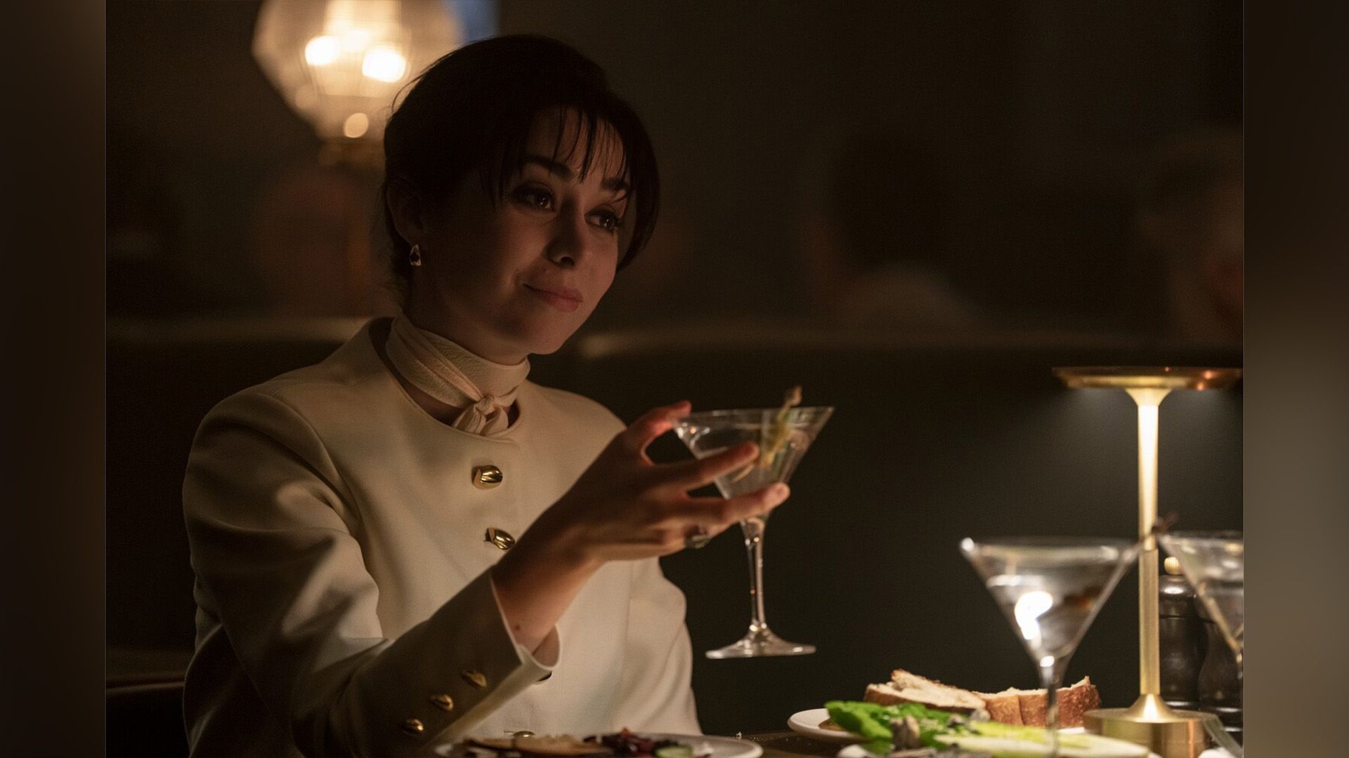 Cristin Milioti con un traje blanco sosteniendo un vaso en un fotograma de la serie "The Penguin"