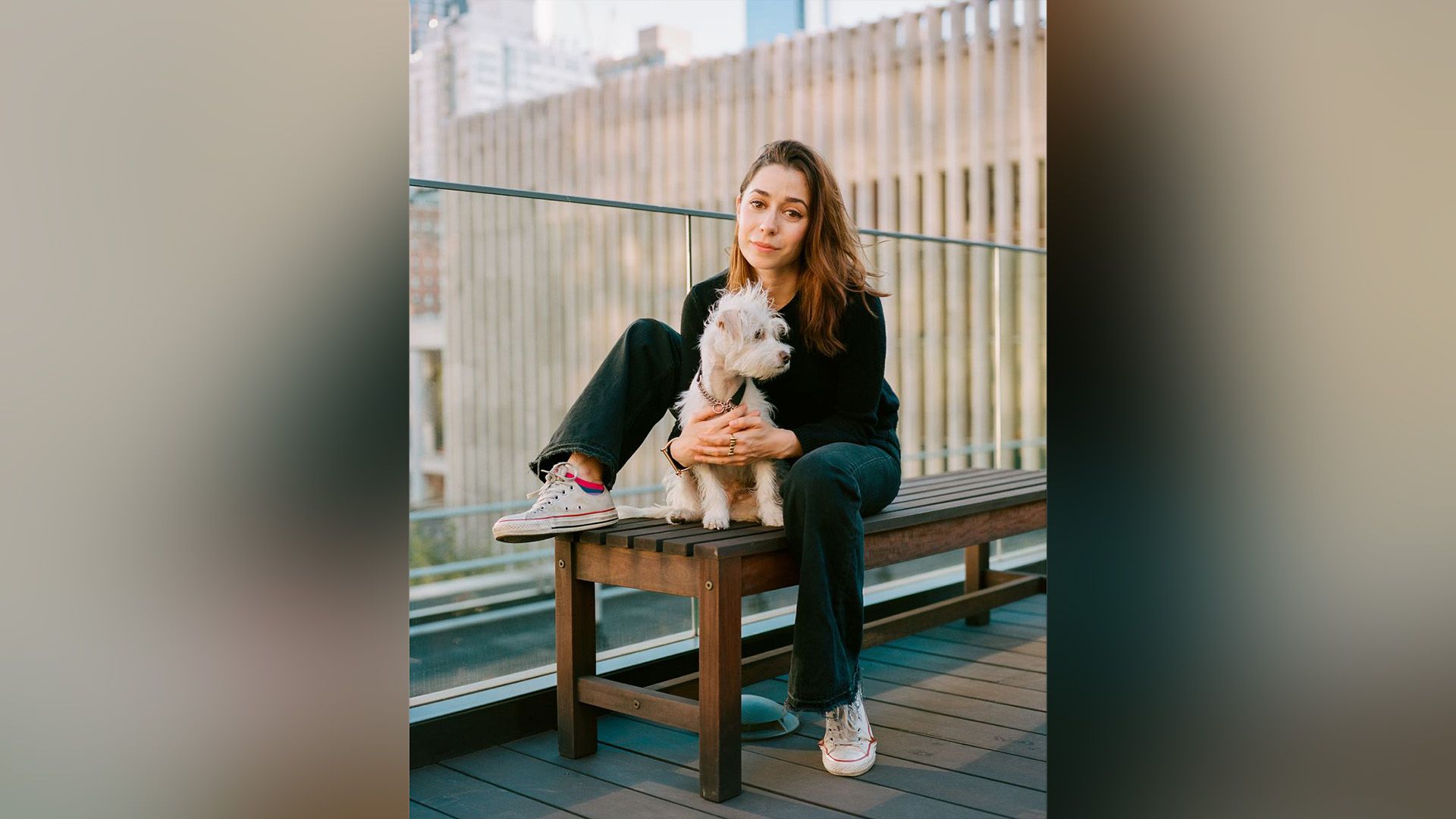Cristin Milioti sentada en un banco, abrazando a un pequeño perro blanco y esponjoso