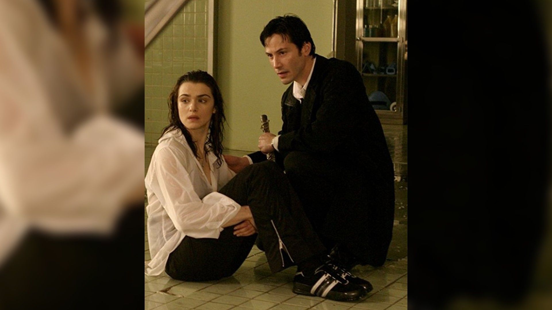 Rachel Weisz y Keanu Reeves sentados en el suelo uno al lado del otro
