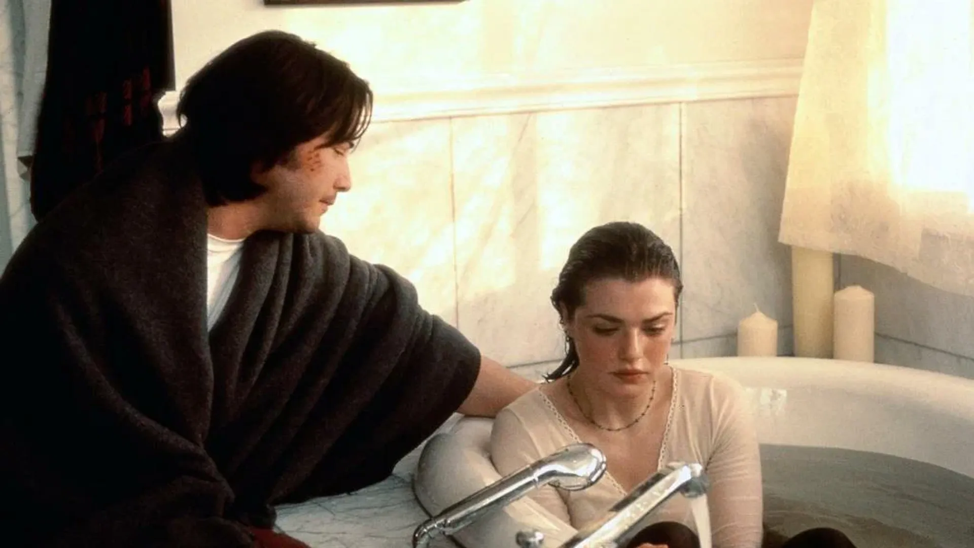La joven Rachel Weisz está sentada en la bañera vestida, a su lado se sienta el joven Keanu Reeves