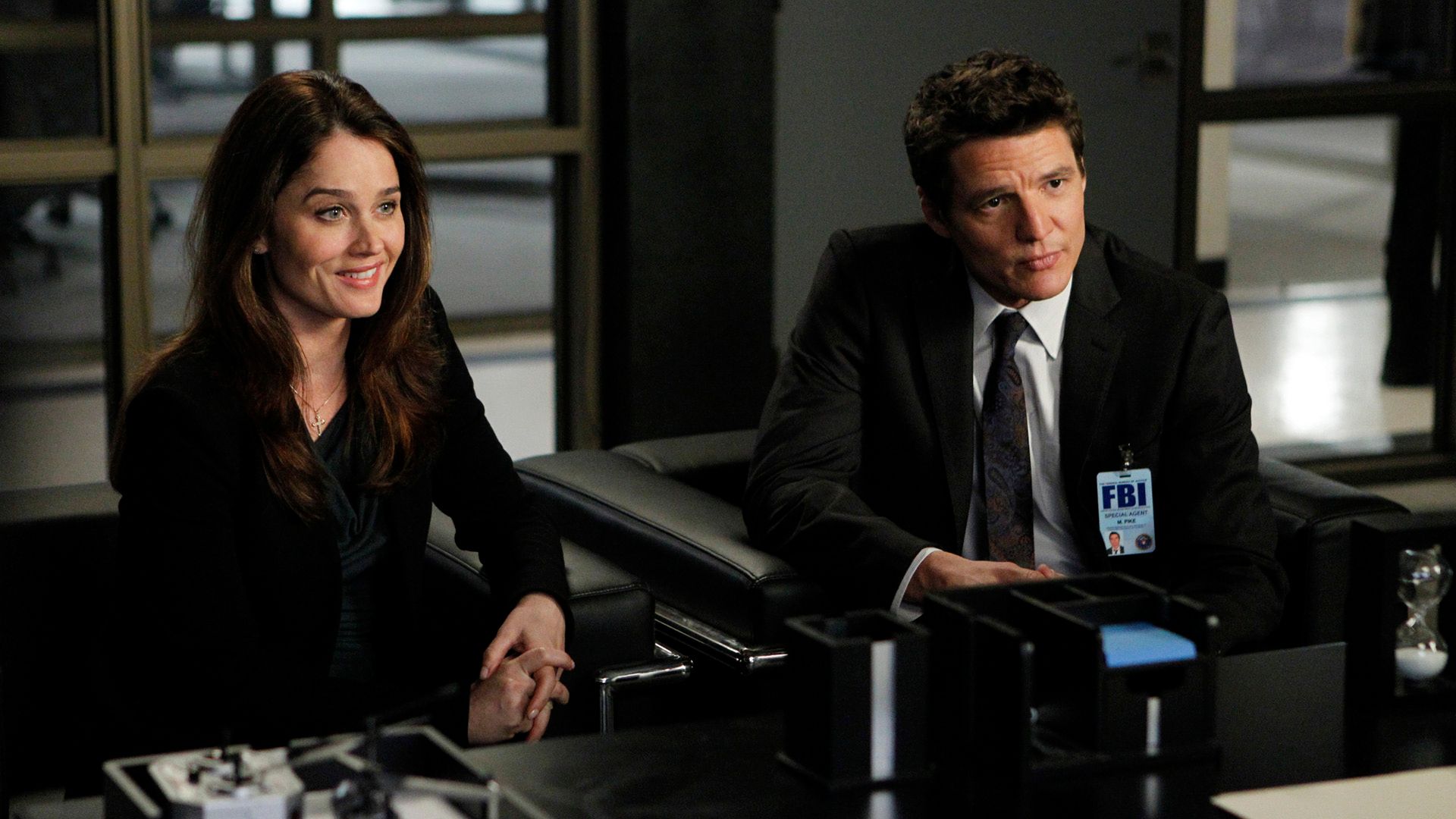 Pedro Pascal con una placa de agente del FBI y Robin Tunney sentados en una mesa en la serie "The Mentalist"