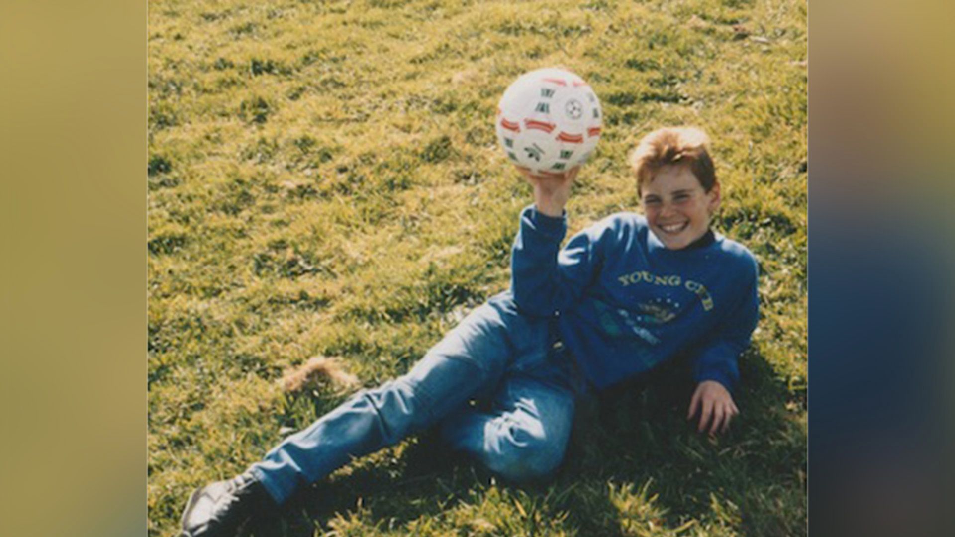 Joven Michael Fassbender yace sobre el césped, sosteniendo una pelota de fútbol en una mano