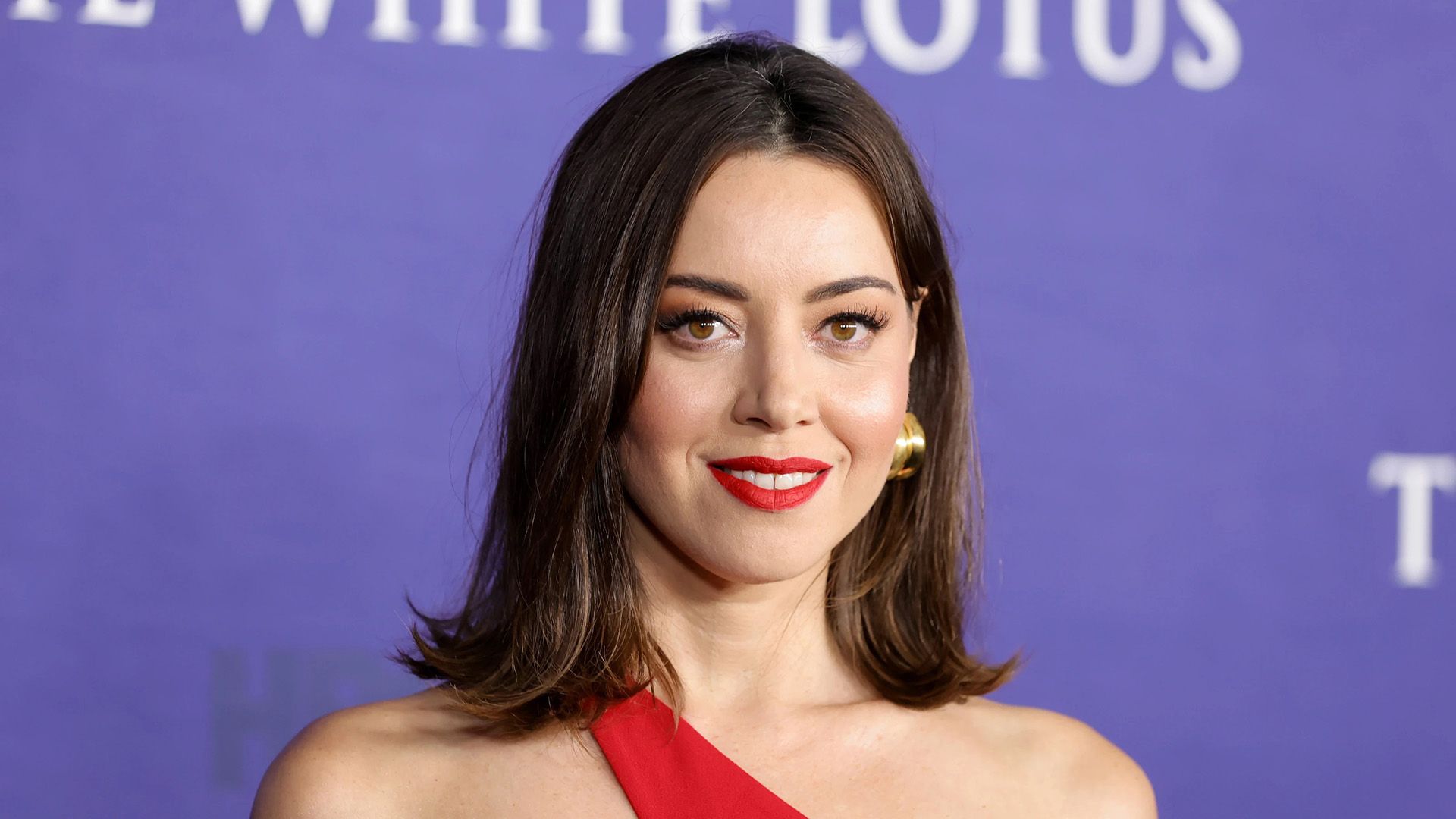 Actress Aubrey Plaza in a red dress on a purple background