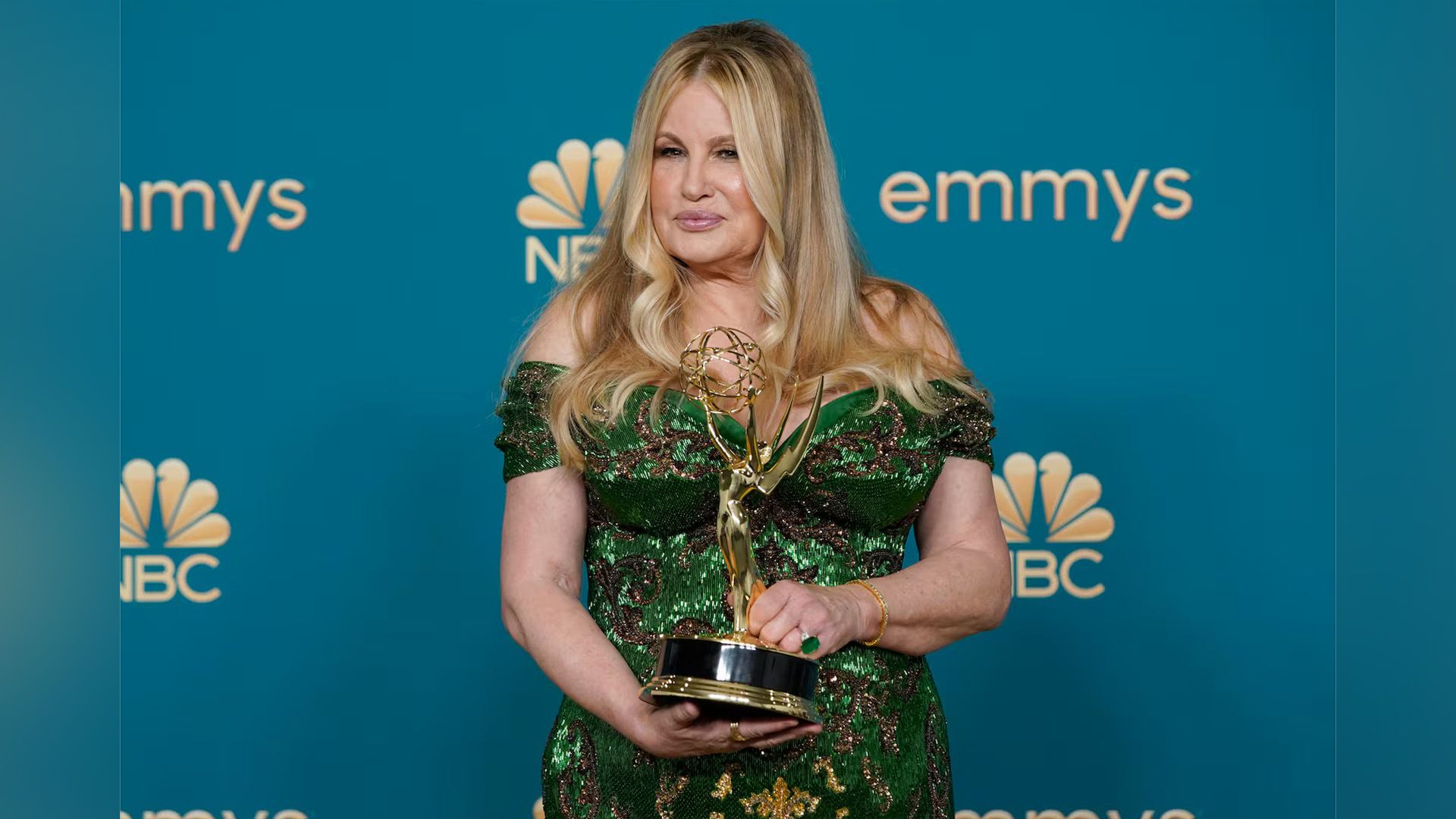 Actriz Jennifer Coolidge con un vestido verde brillante sosteniendo una estatuilla Emmy