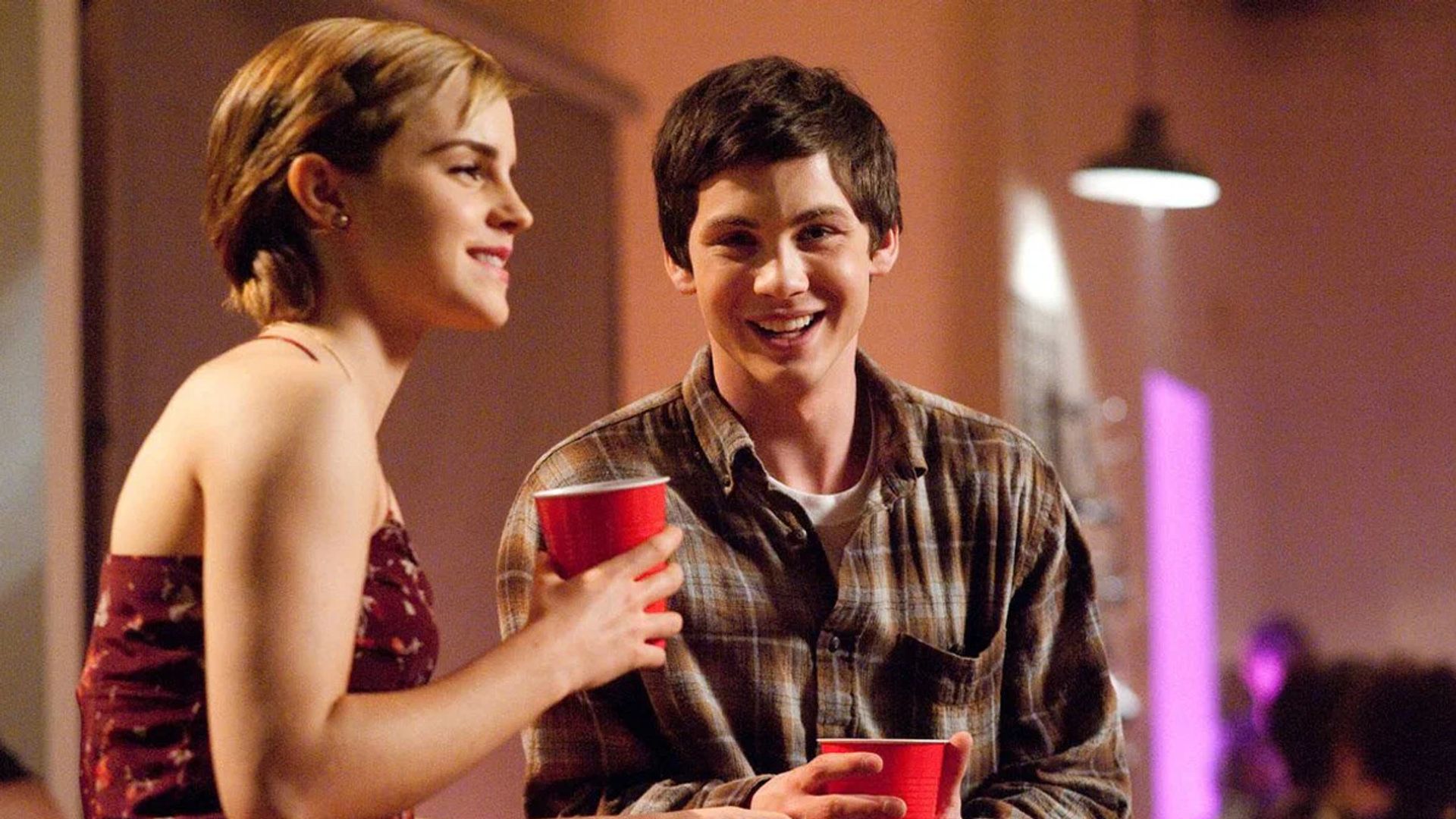 Emma Watson y Logan Lerman sentados a la mesa sosteniendo vasos de plástico