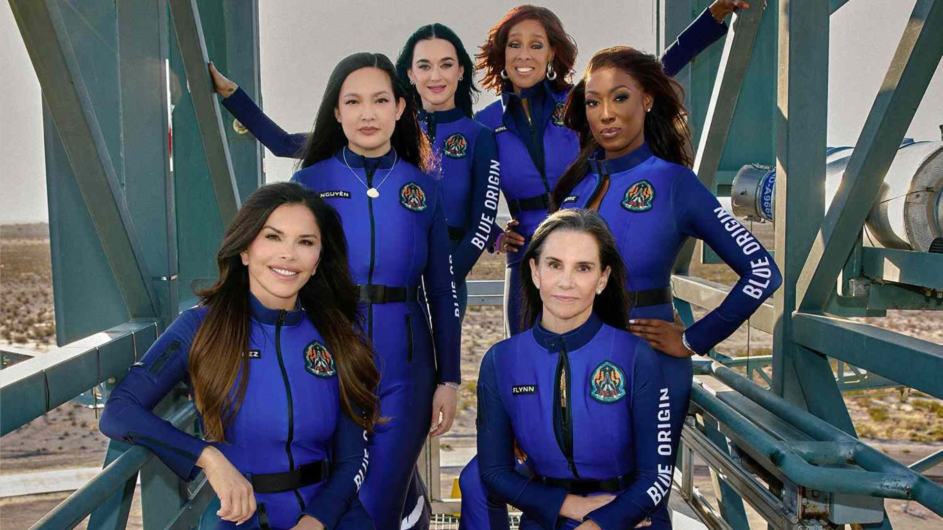 Seis mujeres en trajes espaciales azules posan y sonríen en el ascensor