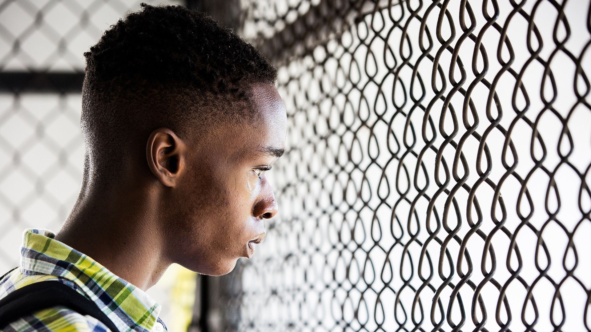 Ashton Sanders con una camisa a cuadros mira a través de la malla de hierro