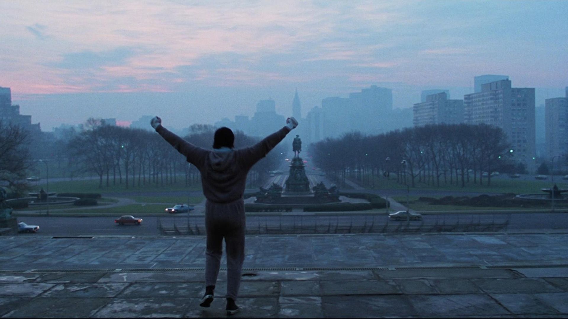 Un joven Sylvester Stallone está en la plaza de la ciudad levantando las manos