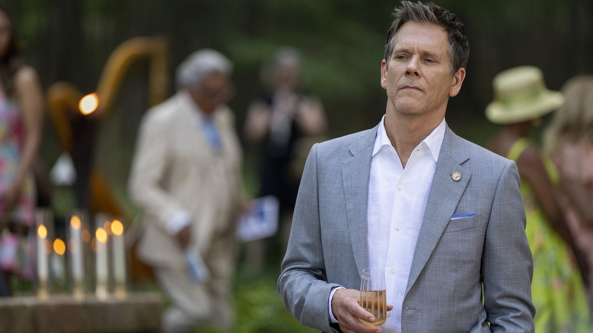 Actor Kevin Bacon en una chaqueta gris y sosteniendo un vaso
