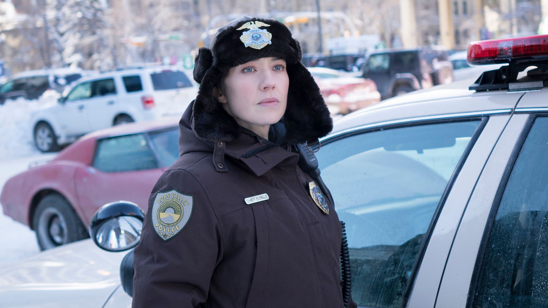 Carrie Coon en un uniforme de policía de invierno junto a un coche de policía
