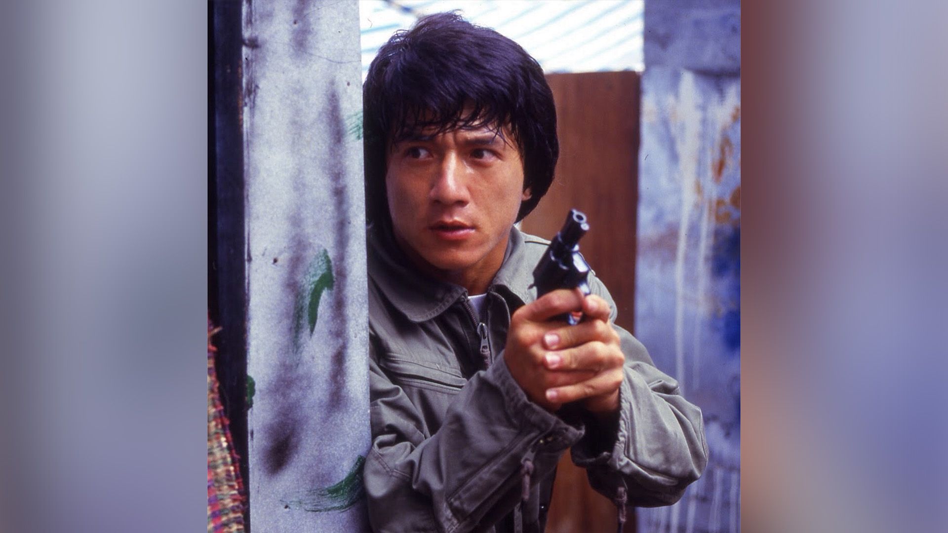 Joven Jackie Chan con una pistola en sus manos asomándose por la esquina en una escena de la película 'Police Story'