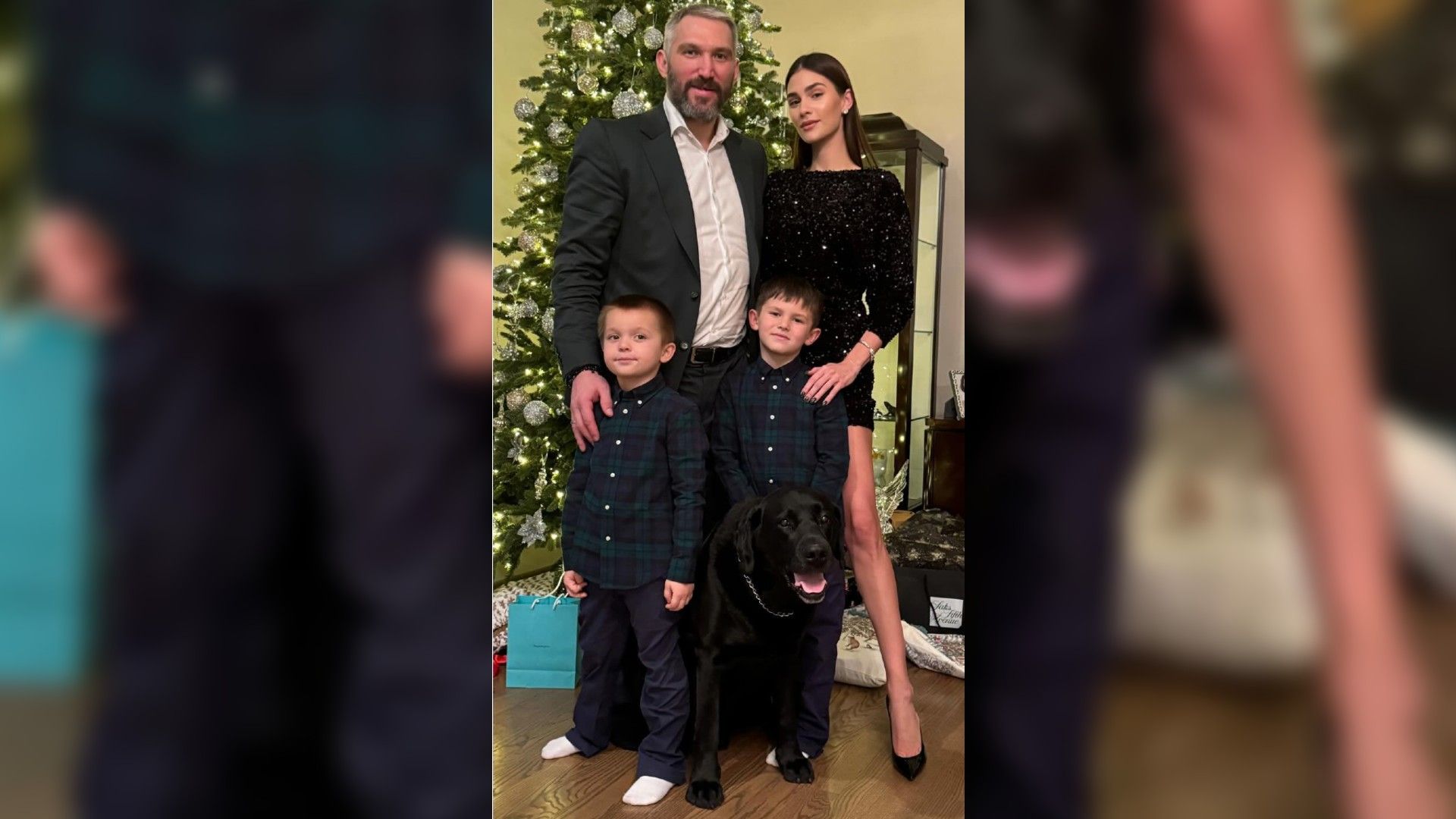 Aleksandr Ovechkin y Anastasia Shubskaya con dos niños y un perro negro posan junto al árbol de Año Nuevo, los padres están vestidos festivamente