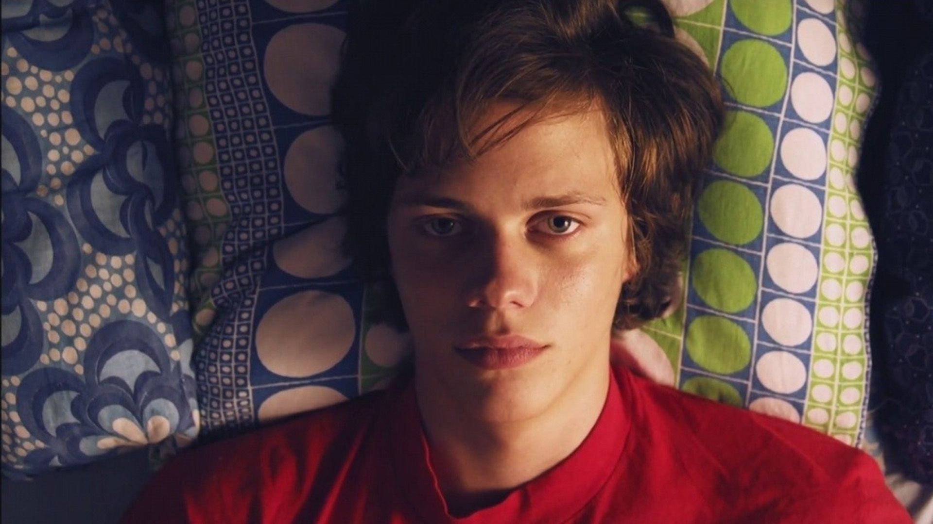 Joven Bill Skarsgård en una camiseta roja acostado en la cama