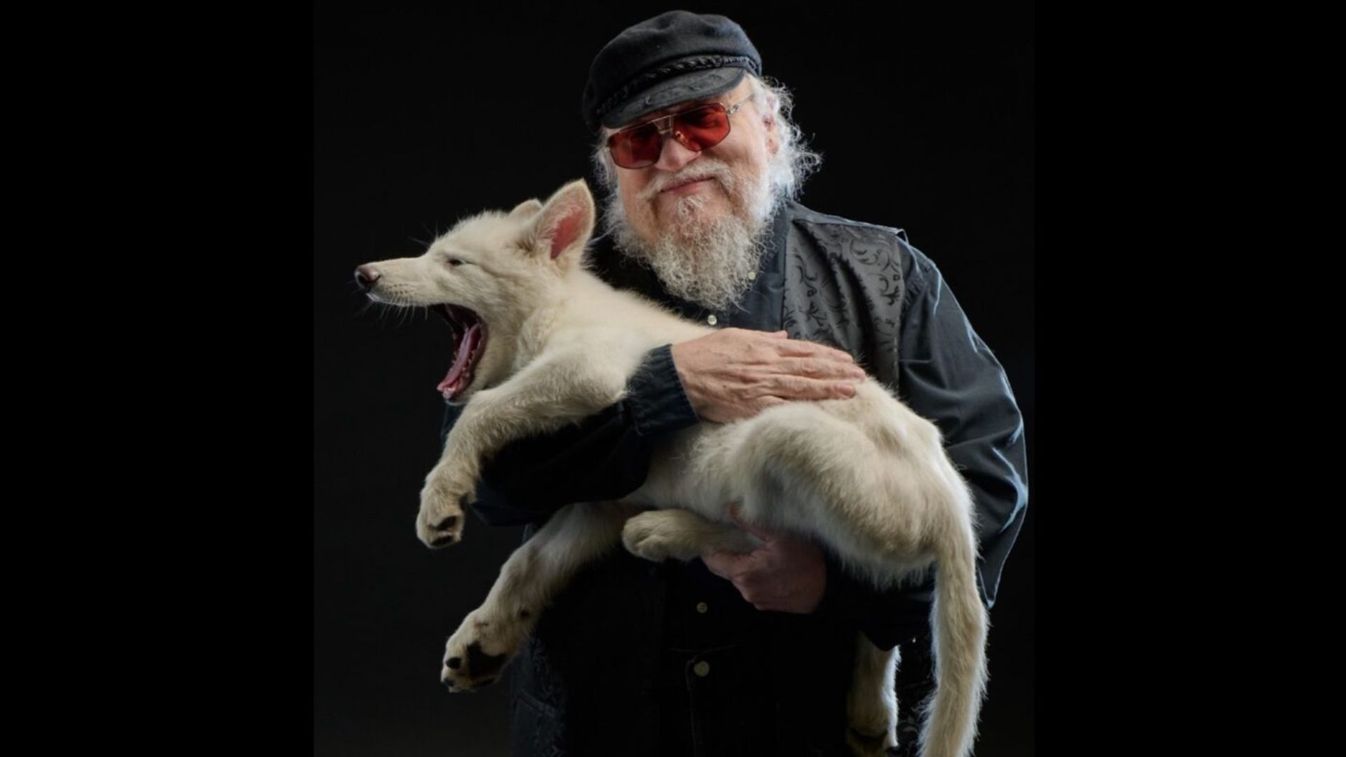 El escritor George Martin sostiene un lobo con la boca abierta y sonríe