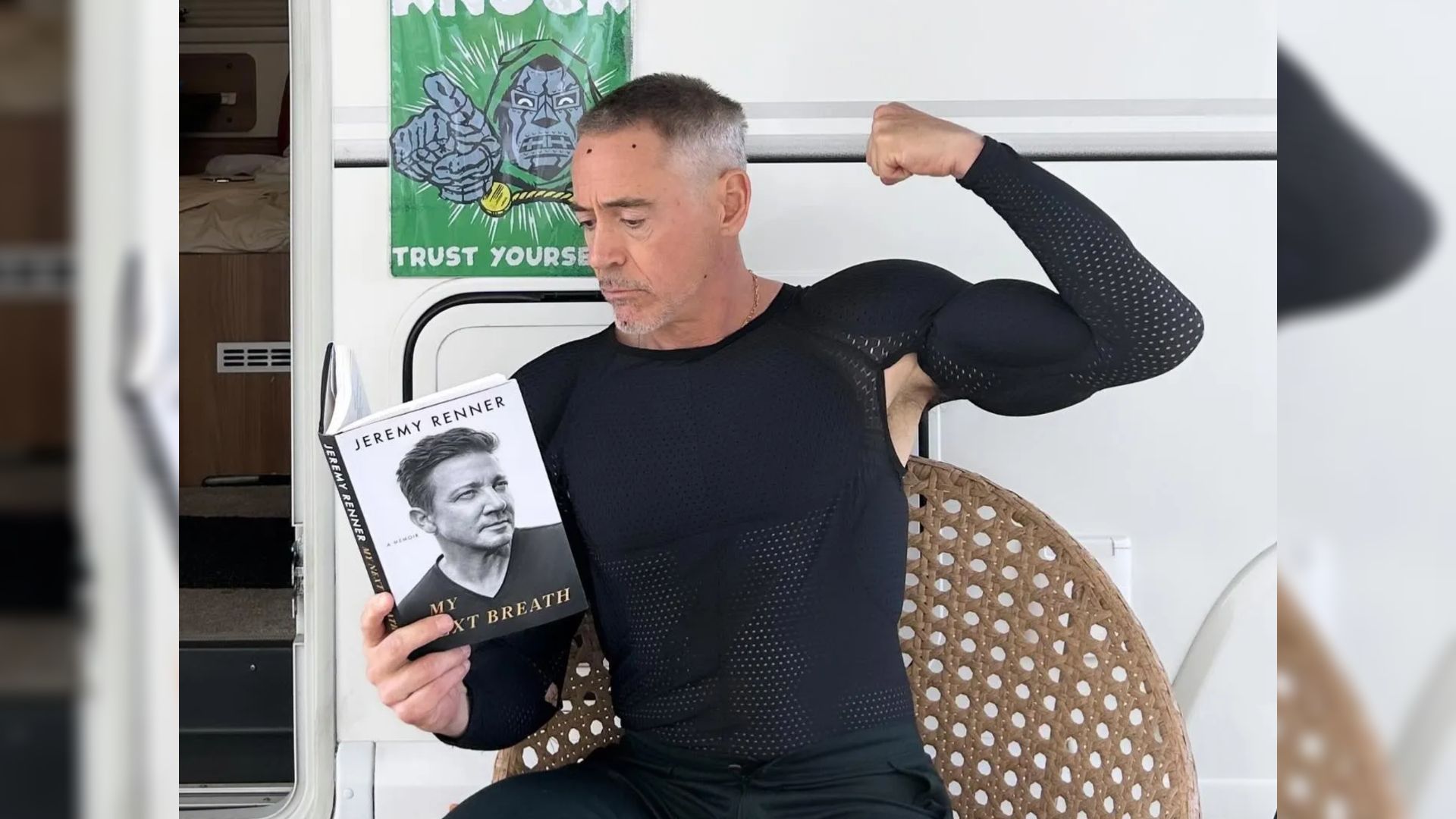 Actor Robert Downey Jr. en ropa ajustada sentado junto a un tráiler y sosteniendo un libro en sus manos
