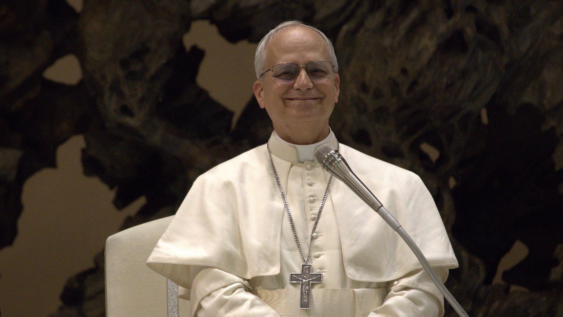 El Papa León XIV sonriendo con vestimenta blanca sobre un fondo oscuro