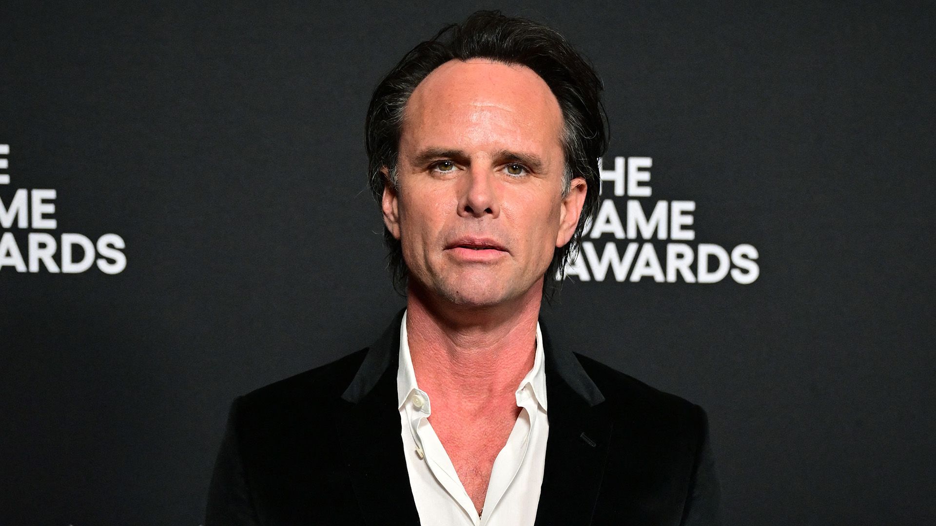 Actor Walton Goggins con una chaqueta negra y camisa blanca con el cuello desabrochado sobre un fondo negro