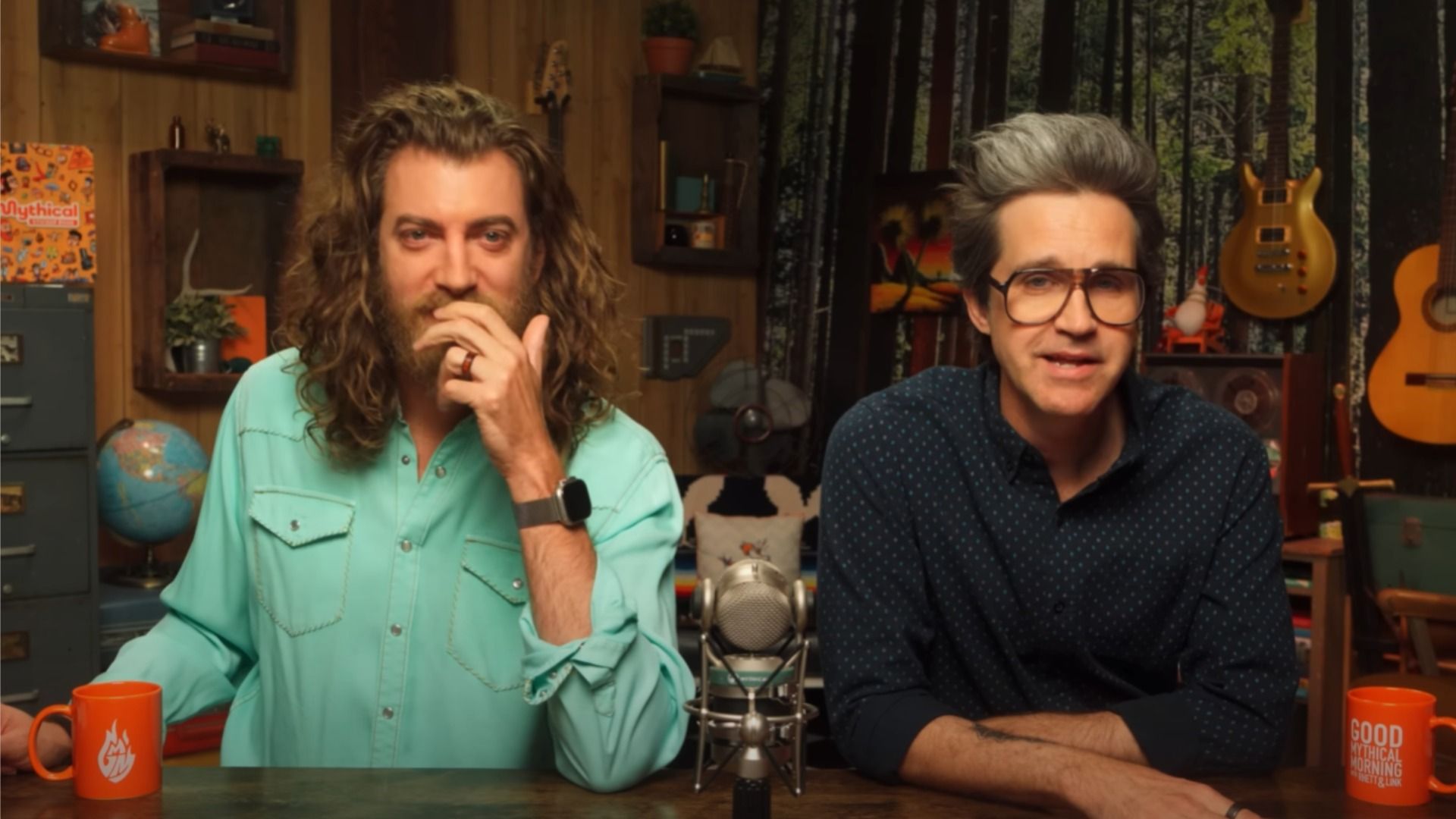 Los bloggers Rhett y Link con camisas sentados en una mesa junto al micrófono