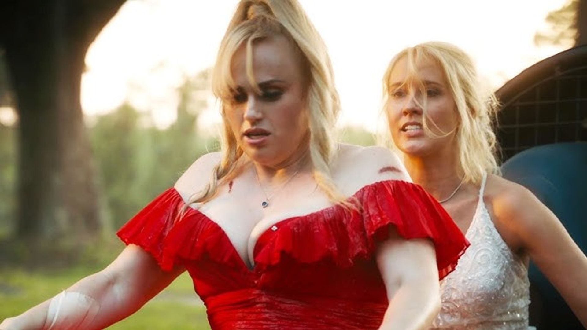 Rebel Wilson en vestido rojo y Anna Camp en blanco montando bicicletas