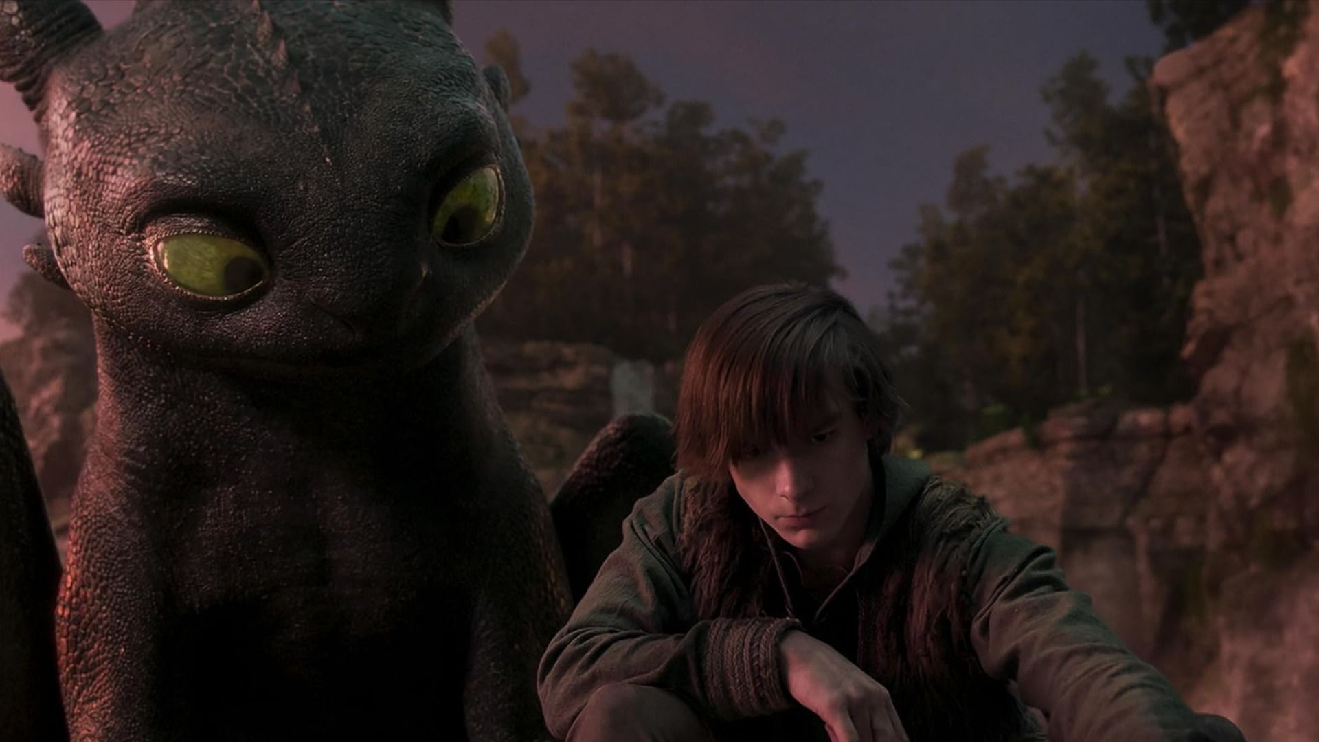 Un chico con ropa gris se sienta junto a un dragón negro con ojos verdes