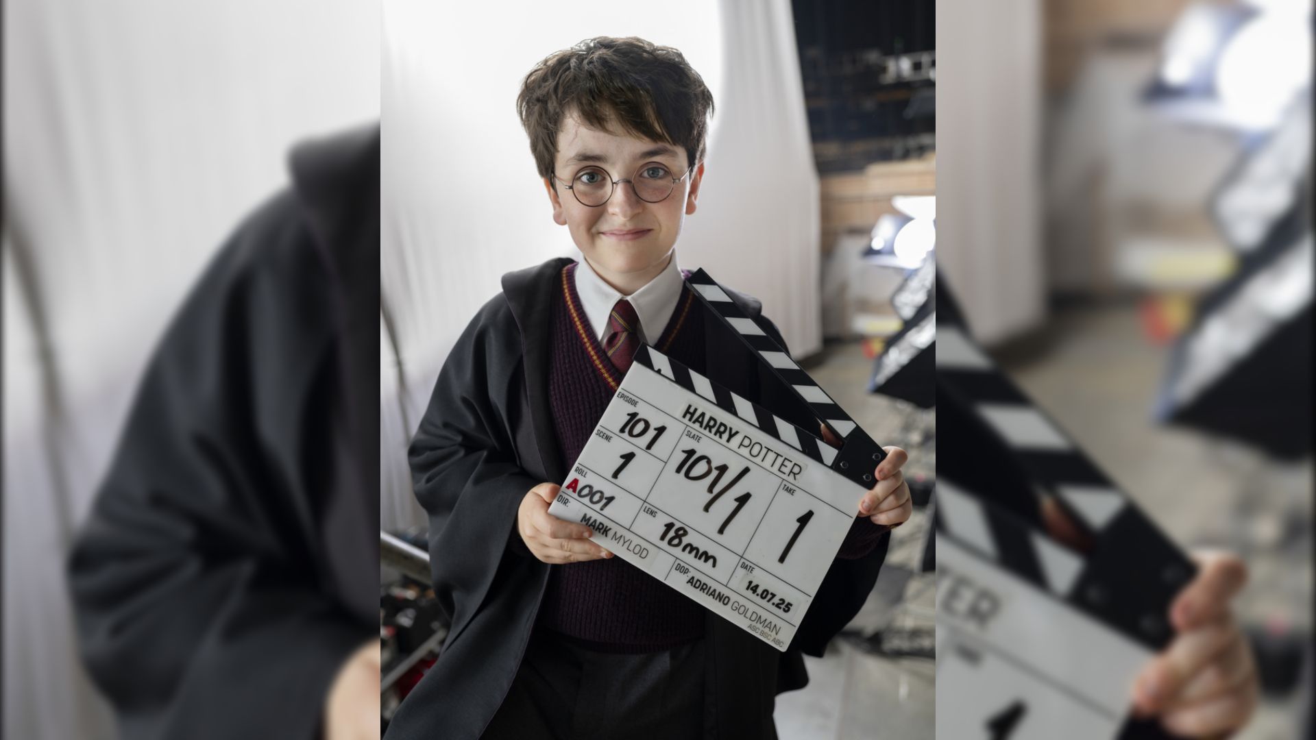 El actor Dominic McLaughlin con capa negra y gafas sostiene una claqueta de filmación