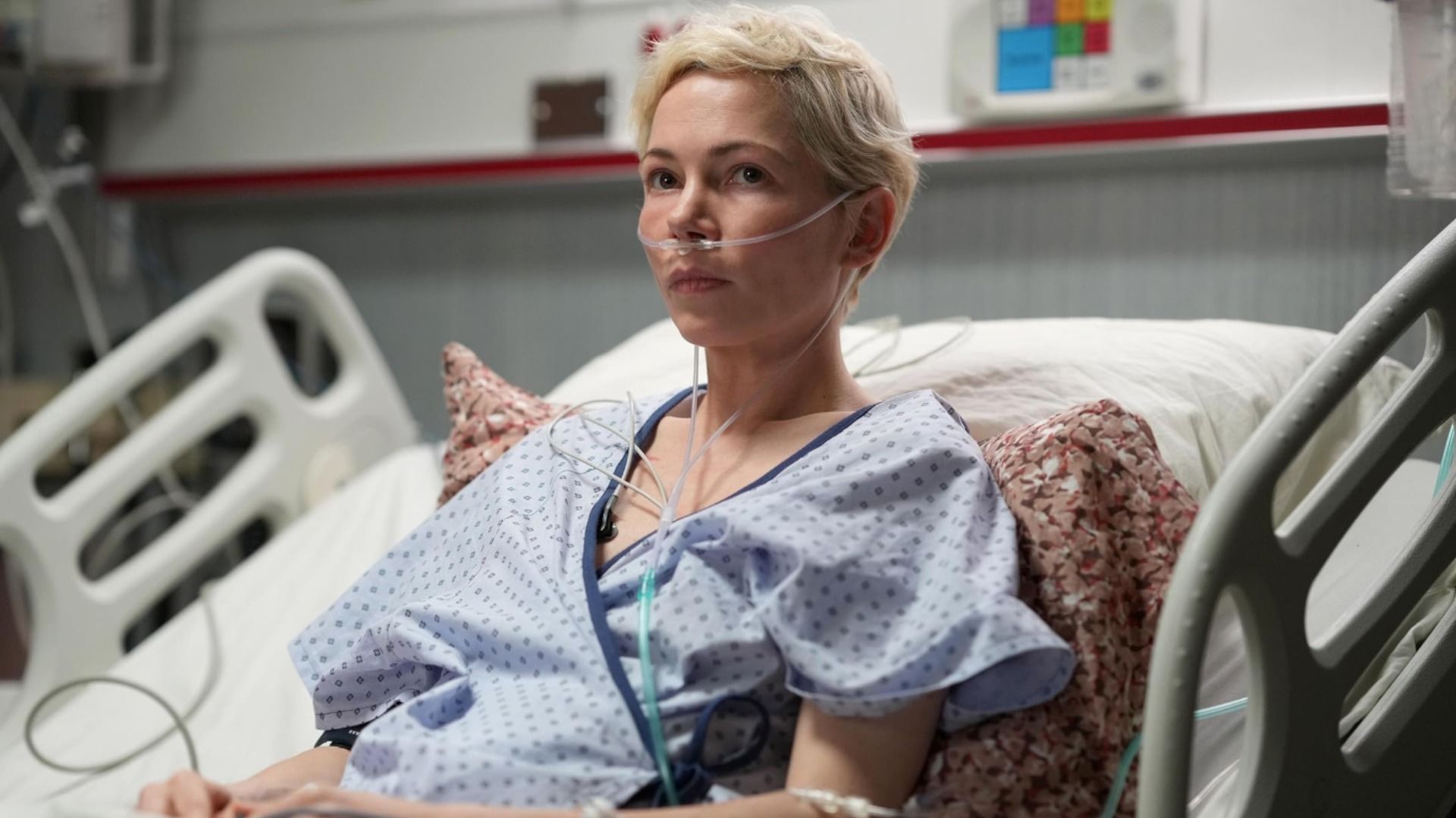 La actriz Michelle Williams con ropa de paciente hospitalario yace en una cama con un tubo en la nariz