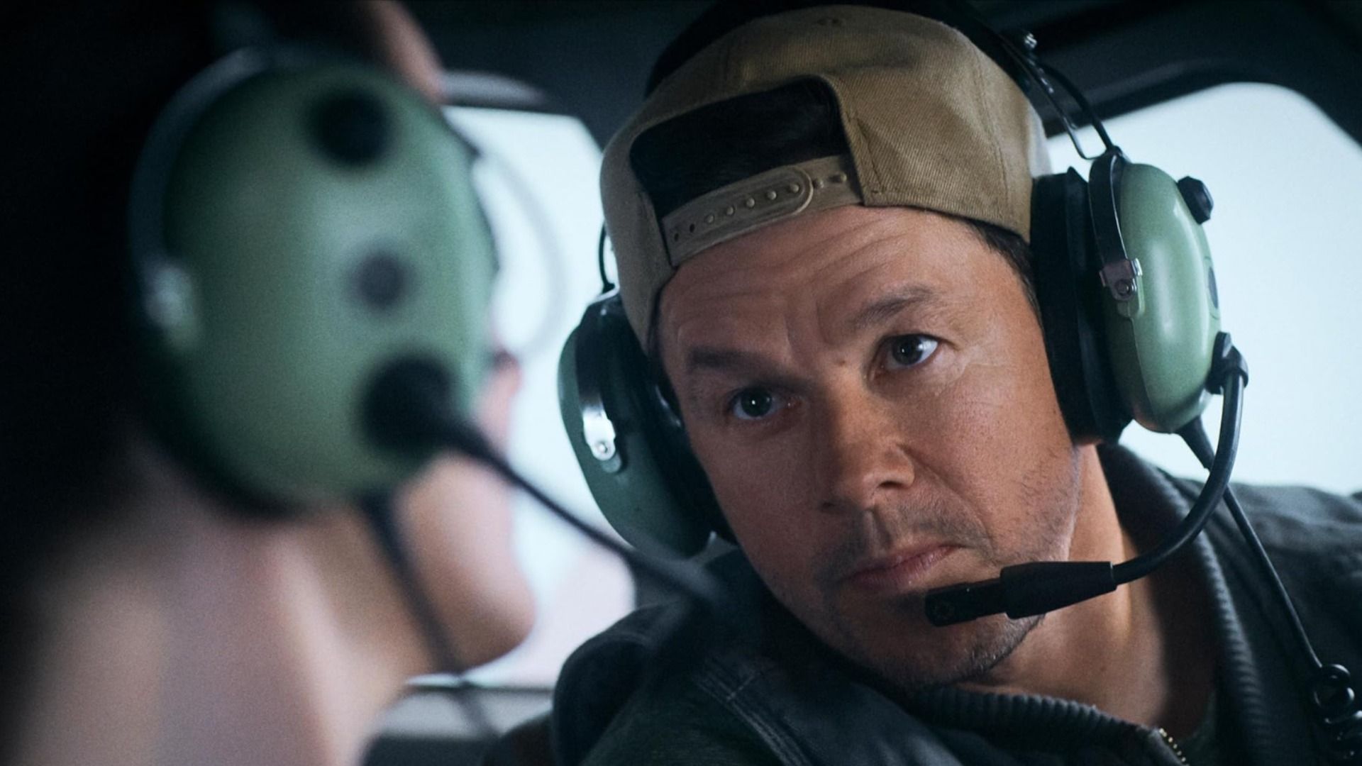 El actor Mark Wahlberg con gorra y auriculares con micrófono sentado en un avión