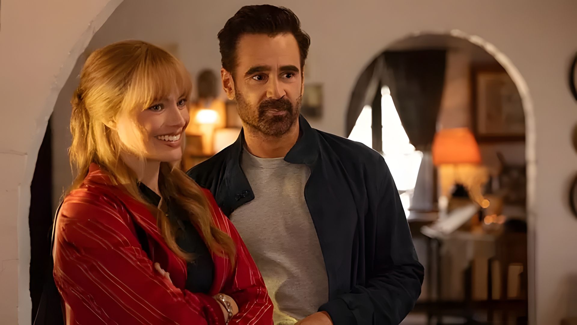 Margot Robbie y Colin Farrell de pie uno al lado del otro en una habitación acogedora con iluminación suave y cálida