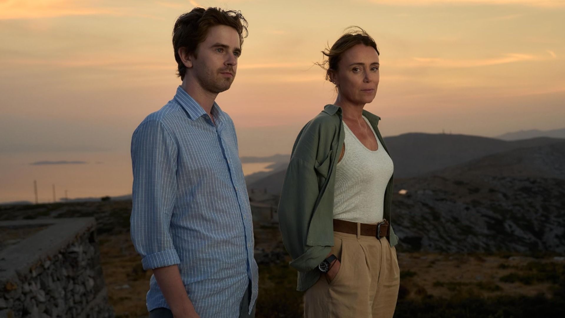 El actor Freddie Highmore con camisa azul y la actriz Keeley Hawes con camiseta blanca parados contra un fondo montañoso