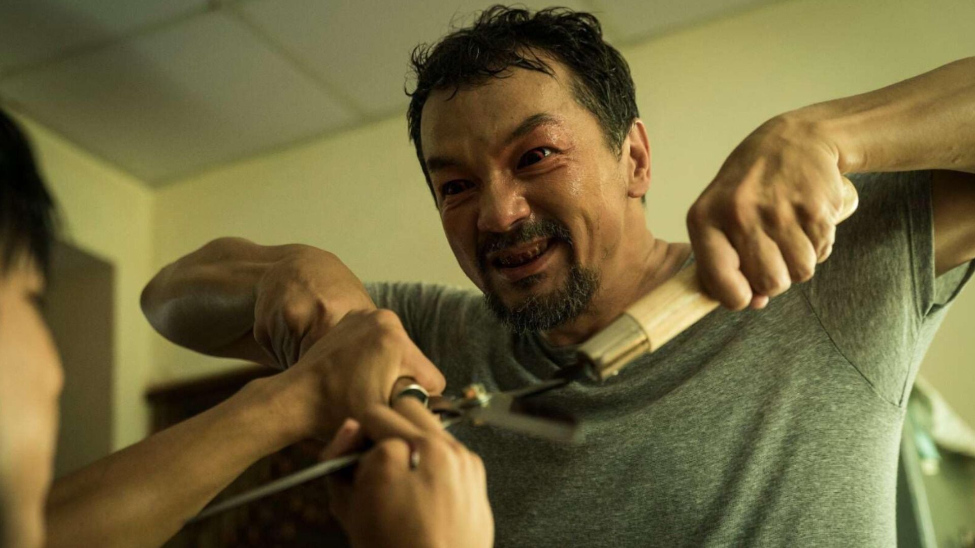 Un hombre con camiseta gris y ojos rojos sosteniendo tijeras de podar