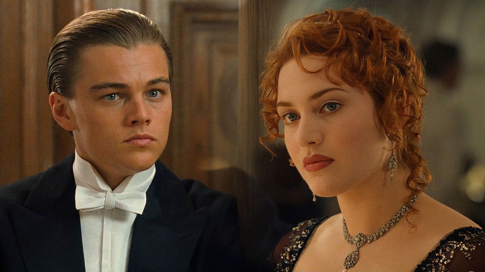 El actor Leonardo DiCaprio con esmoquin y la actriz Kate Winslet con vestido negro de pie contra un fondo marrón