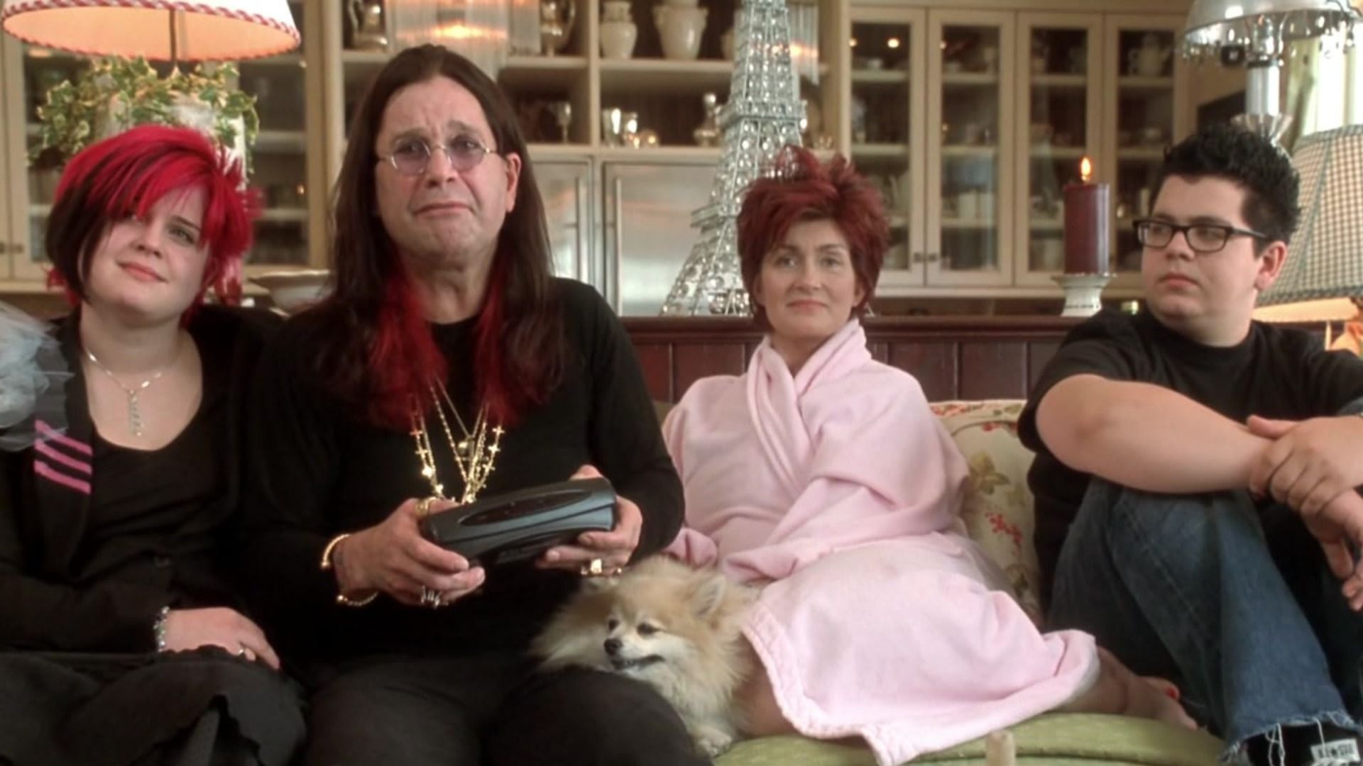 El cantante Ozzy Osbourne con traje negro y cadenas sentado en un sofá con su esposa e hijos